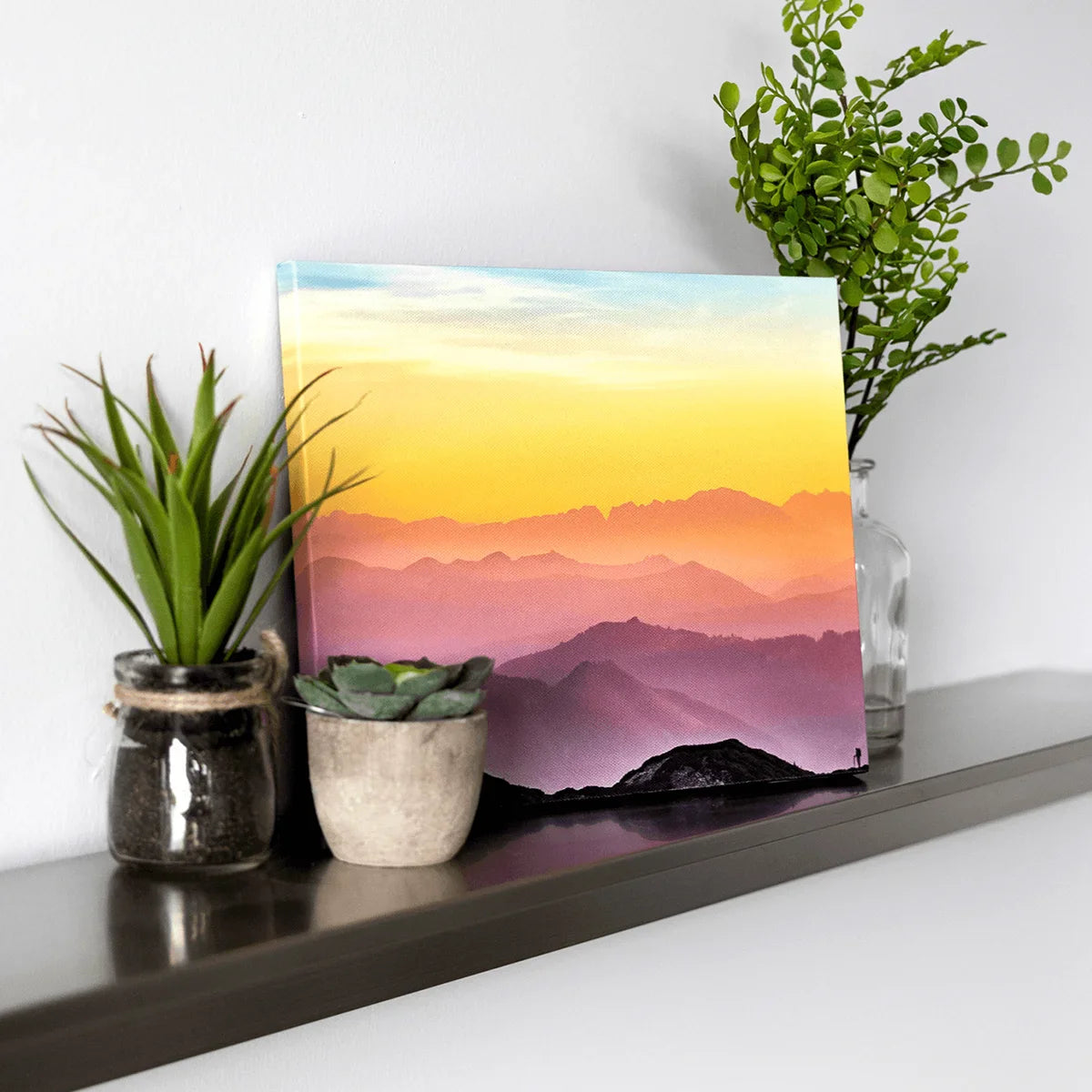 Canvas desk print featuring a colorful mountain sunset, displayed on a shelf with small potted plants.