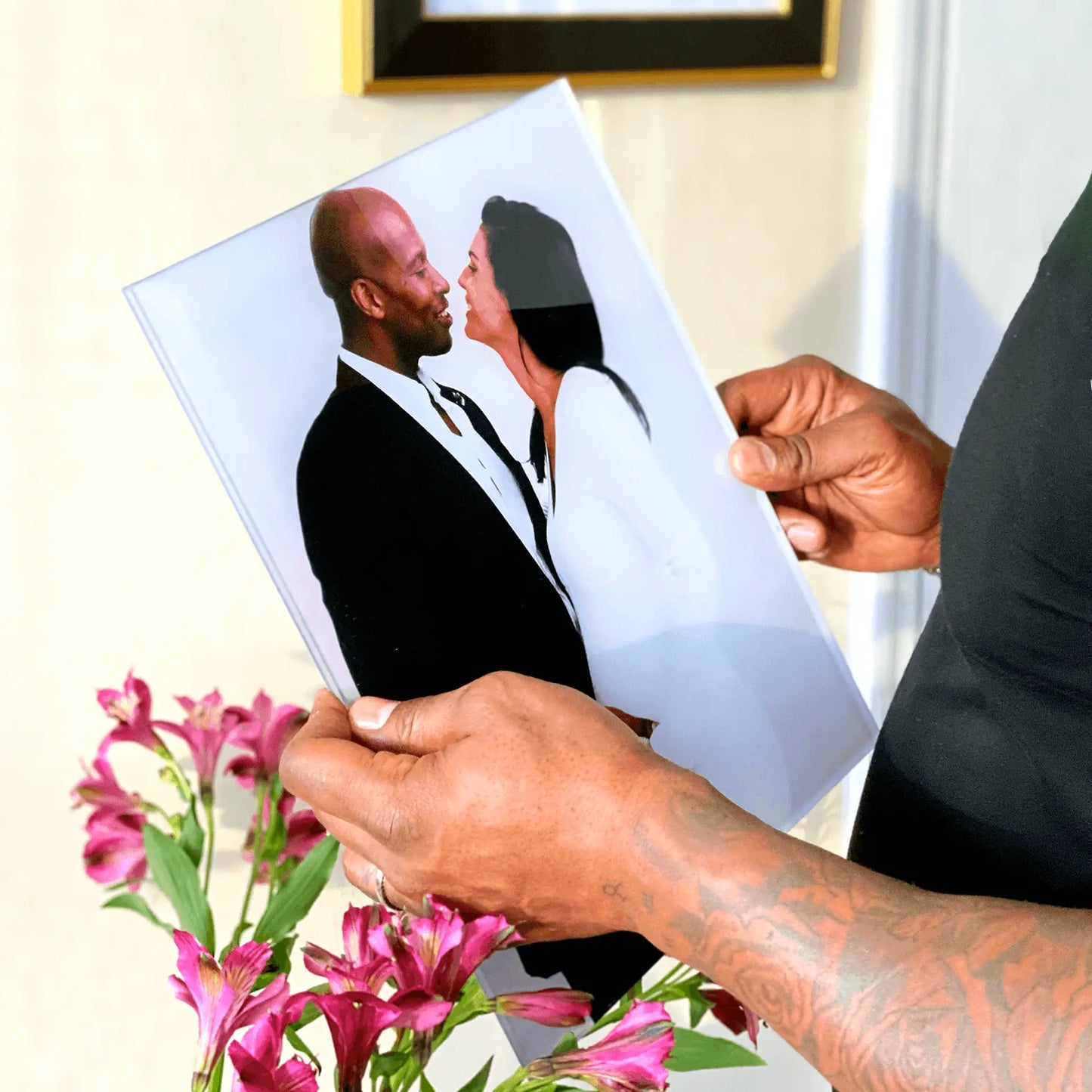 Acrylic wall decor print of a couple facing each other in formal attire, held in hands above pink flowers in an indoor setting.