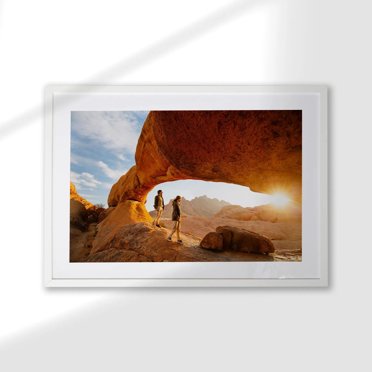 Framed photo print with a white mat, featuring two people walking beneath a natural rock arch at sunset.