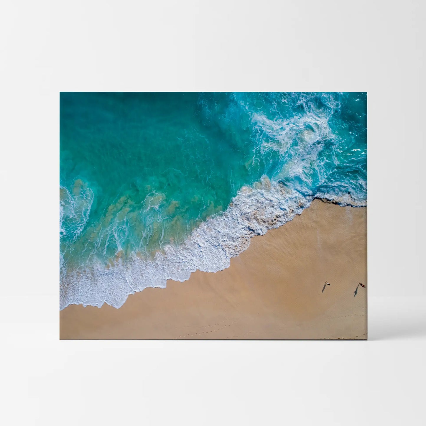 Mounted print with aerial ocean waves in turquoise water meeting sandy beach shoreline, panoramic layout, displayed as frameless wall art.