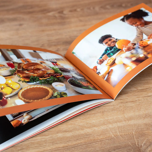 Softcover photo book open to a Thanksgiving spread of turkey and pie, facing a photo of kids helping prepare food in the kitchen.