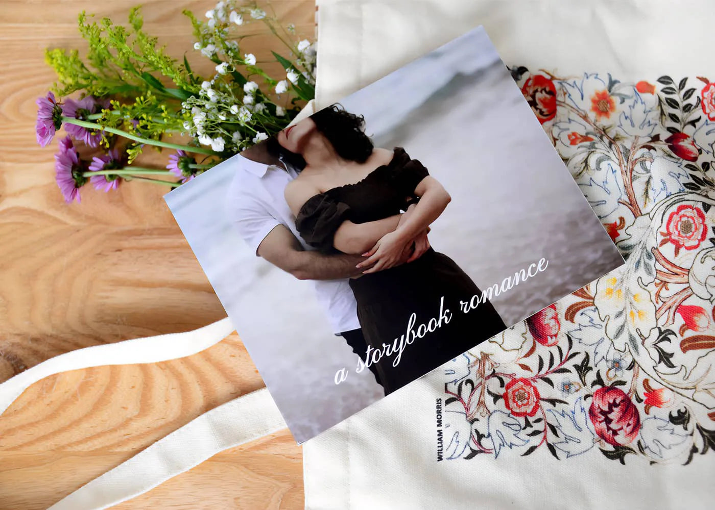 Book titled 'A Storybook Romance' with a couple embracing on the cover, placed on a floral-patterned surface with flowers beside it.