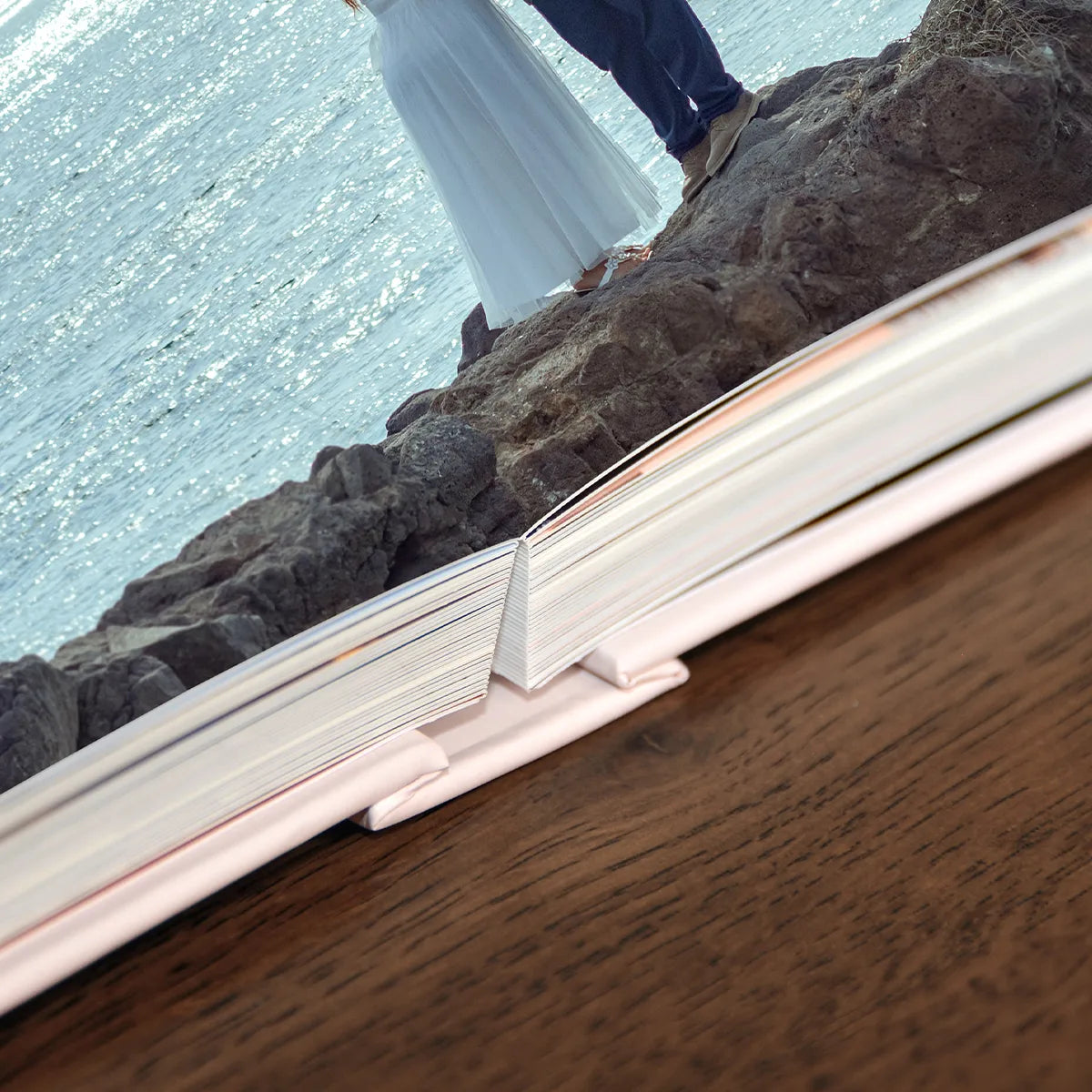 Layflat photo book open to panoramic wedding image, showing seamless center binding and thick, flush-mount pages on wooden table.