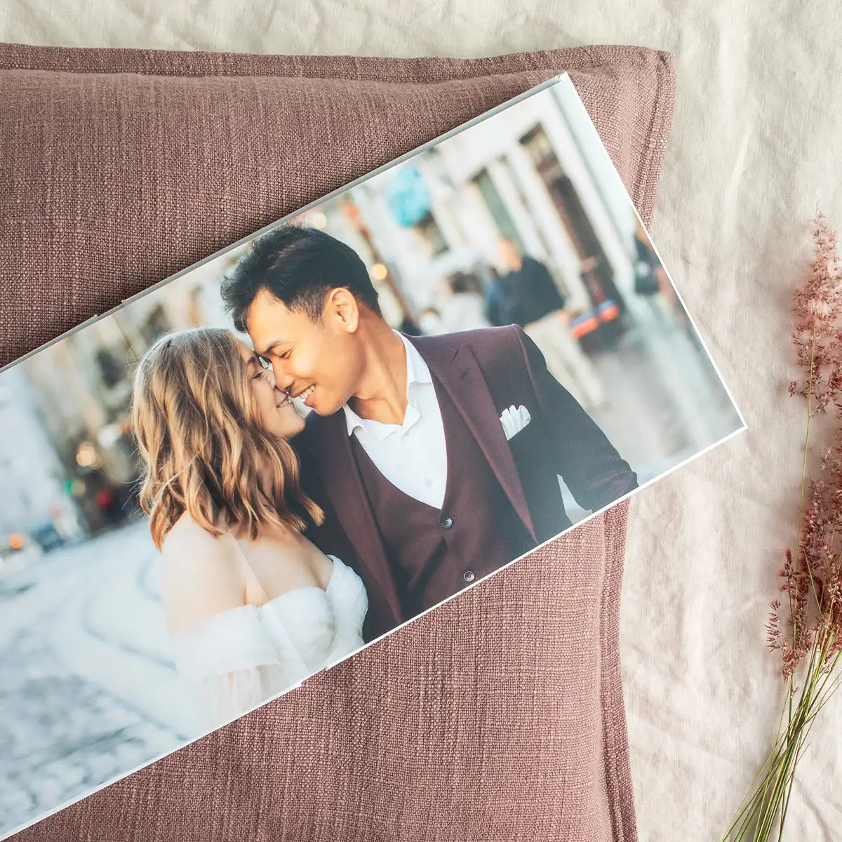 Layflat photo book open to full-bleed wedding portrait spread, resting on textured fabric with soft natural lighting.