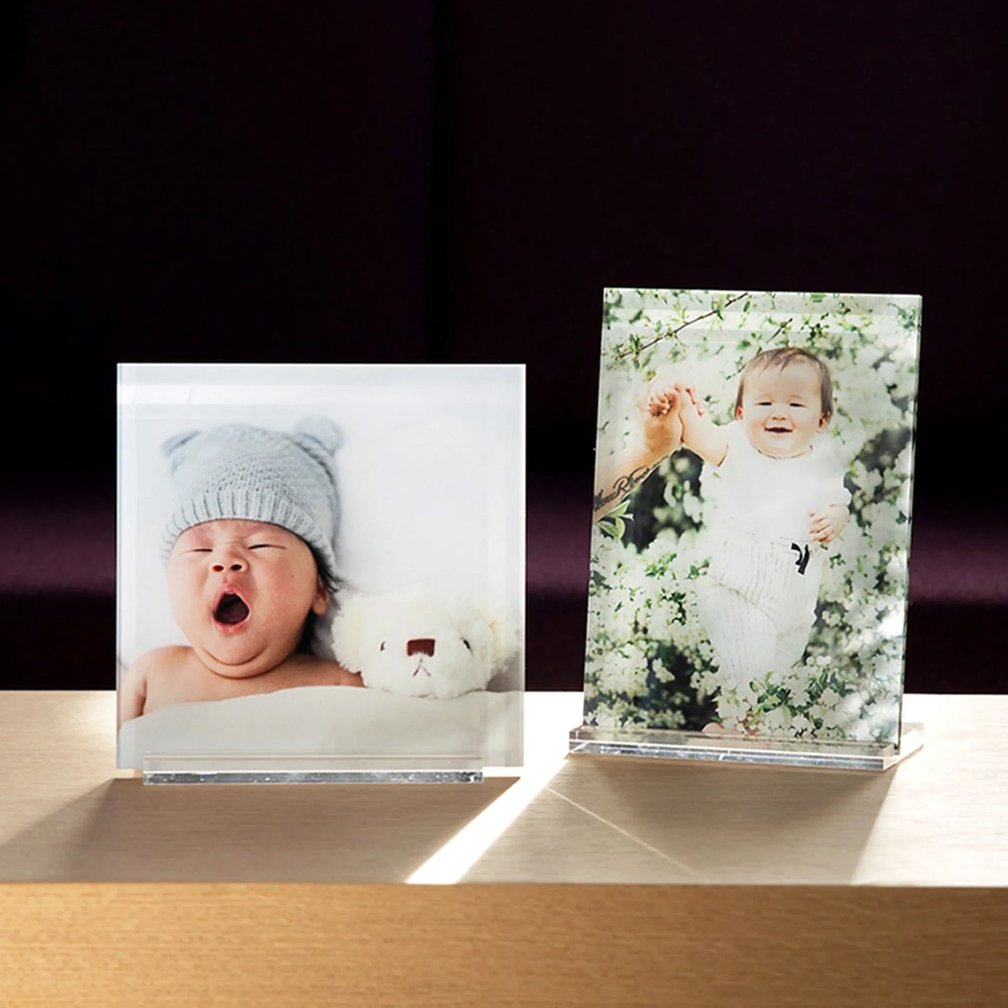 Two acrylic desk prints displayed side by side on a wooden surface, featuring a newborn portrait and a smiling baby in blooming flowers.