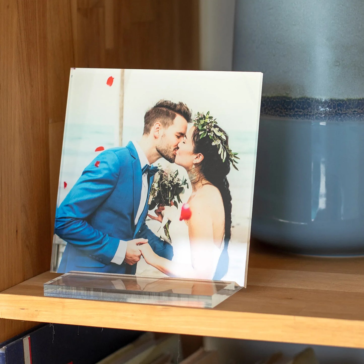 Acrylic desk print of a bride and groom kissing at the beach, displayed upright on a wooden shelf with soft natural light.