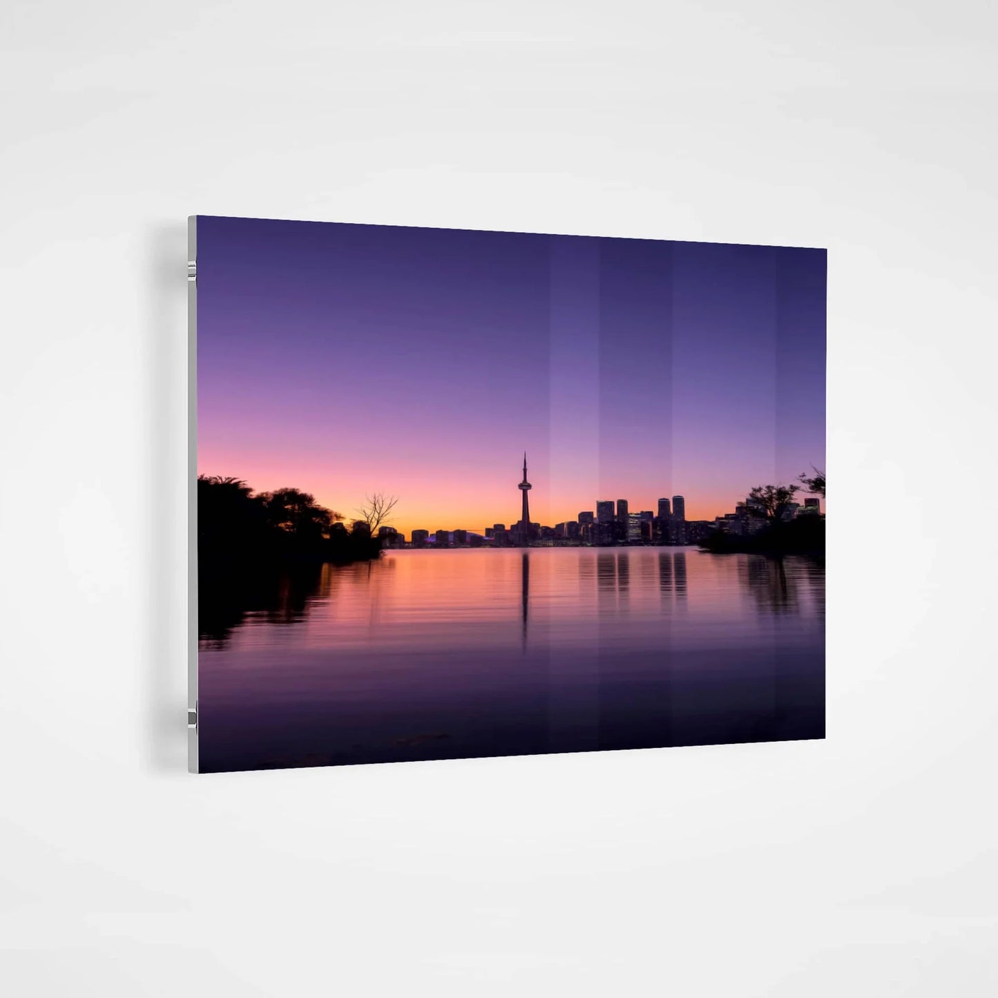 Acrylic wall decor print of a city skyline at sunset reflected on calm water, displayed against a neutral wall with visible side mounting hardware.