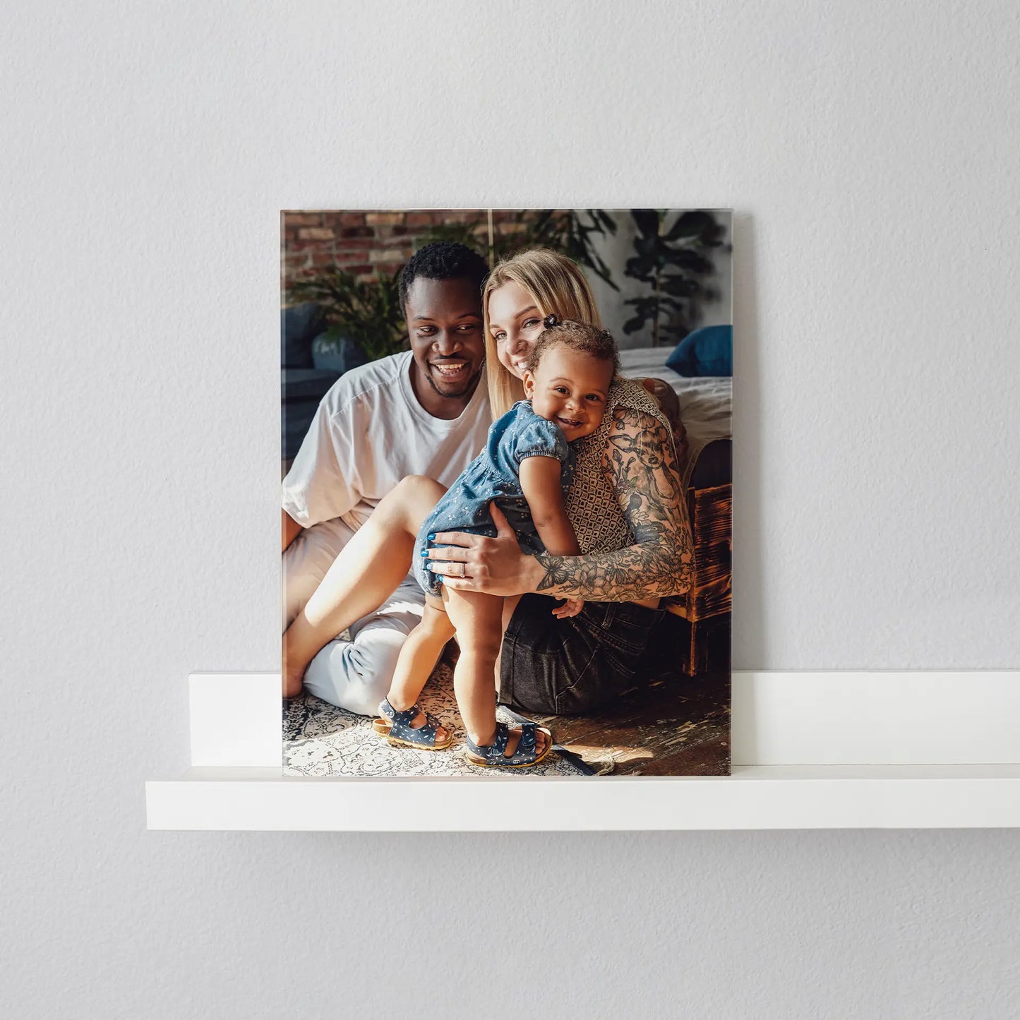 Acrylic print featuring a family with a young child sitting together indoors, displayed on a white floating shelf against a neutral wall.