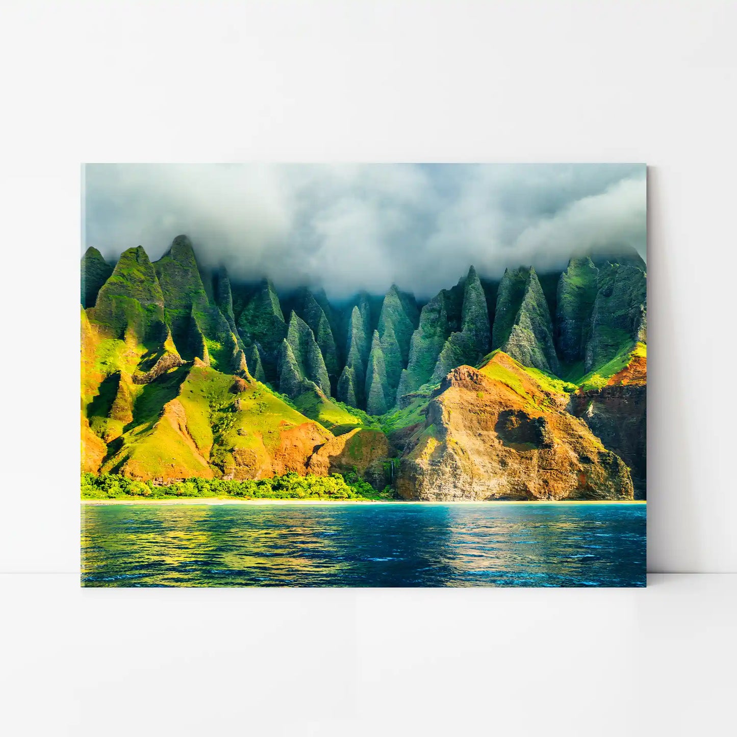Acrylic wall print displaying a tropical coastline with steep green mountains, low clouds, and calm blue water in the foreground.