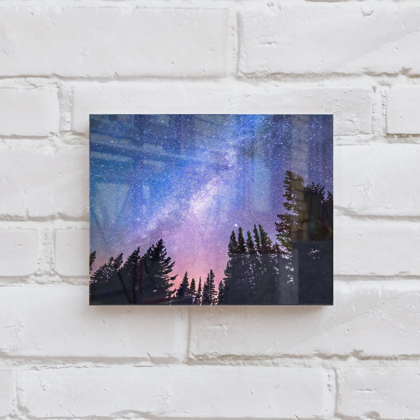 Acrylic wall decor print featuring a star-filled night sky with the Milky Way above silhouetted pine trees, mounted on a white brick wall.