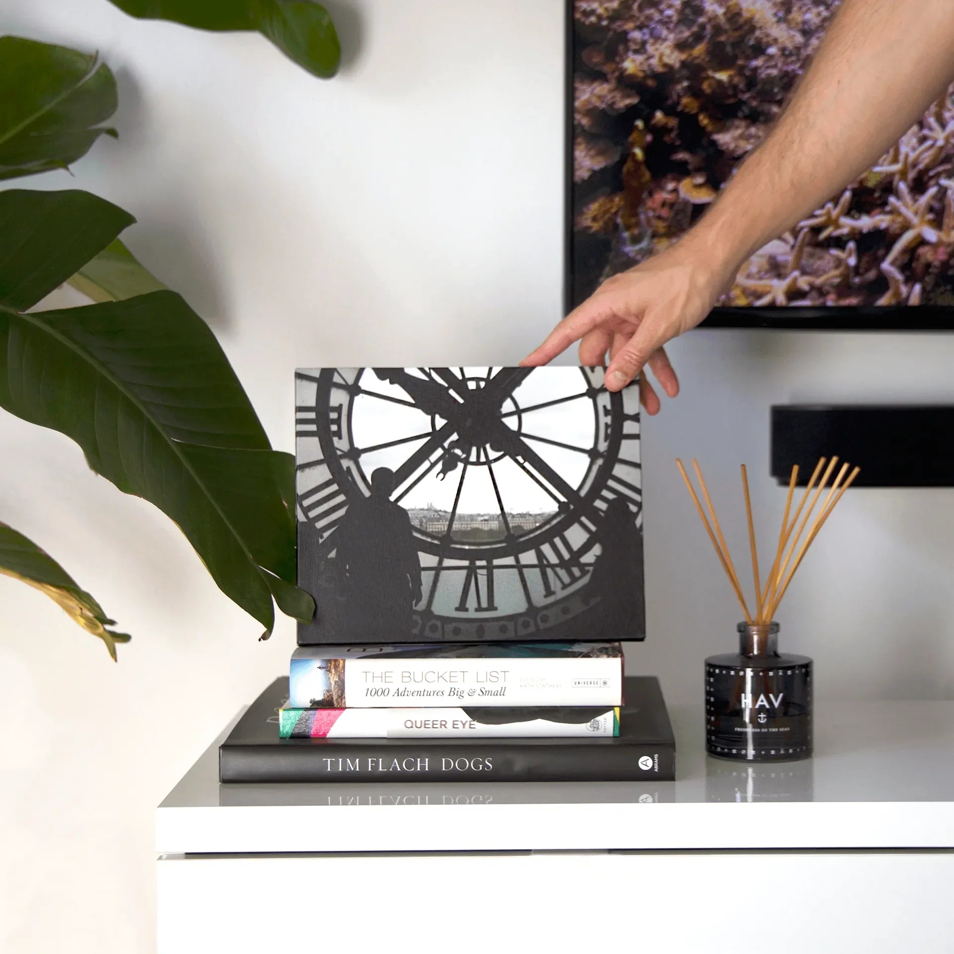 Canvas desk print showing a silhouette of a person inside a large clock tower, styled on stacked books beside a reed diffuser.