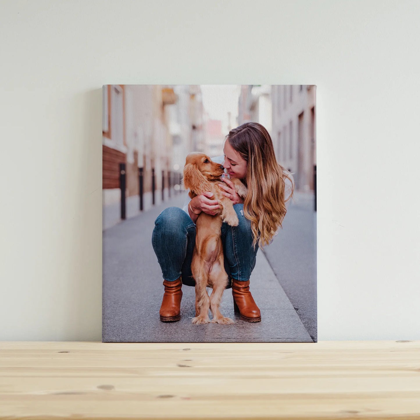 Canvas desk print featuring a woman crouching and holding a small brown puppy on a city street, displayed on a light wood surface.