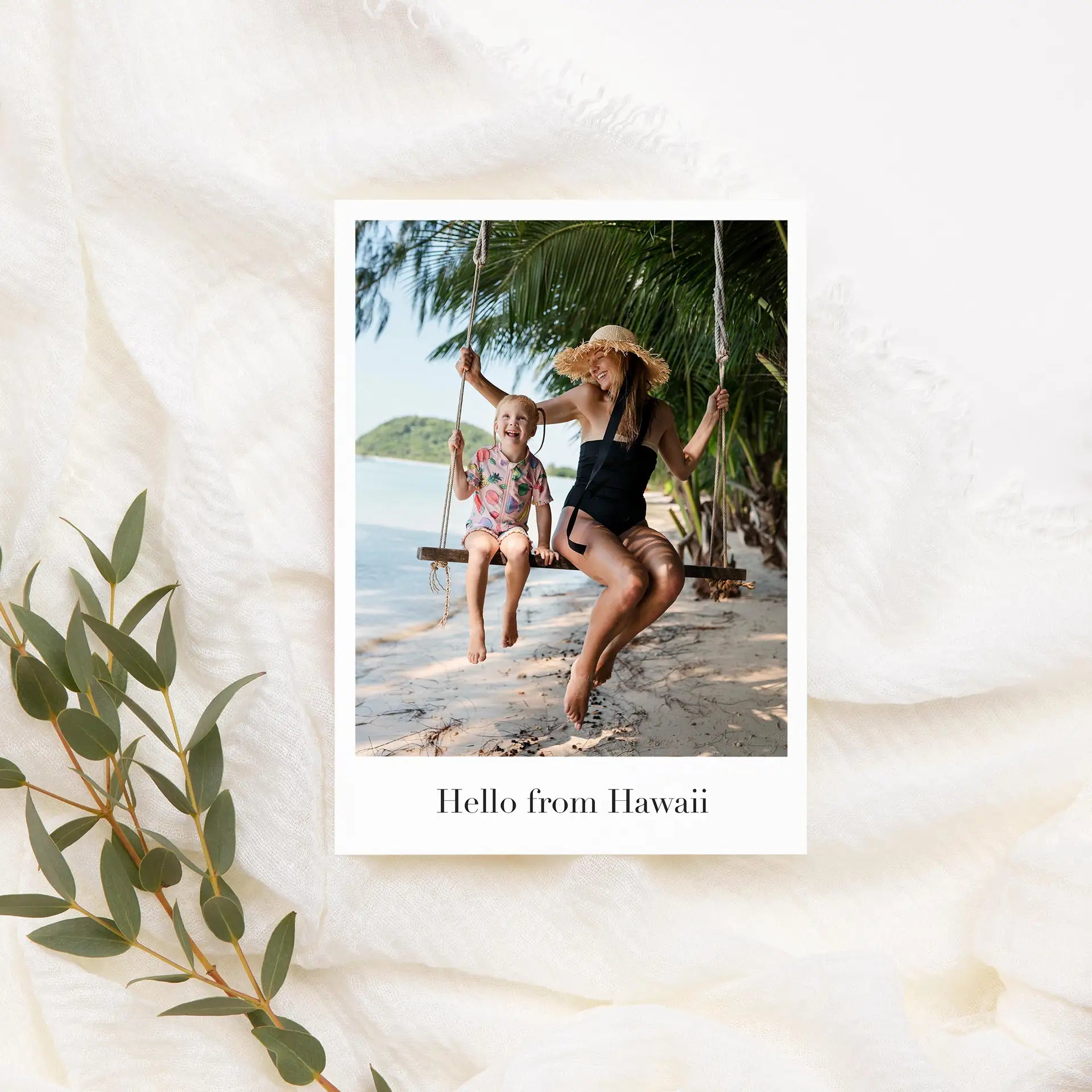 Flat photo card with beach portrait of woman and child on swing under palm trees, text reads “Hello from Hawaii.”
