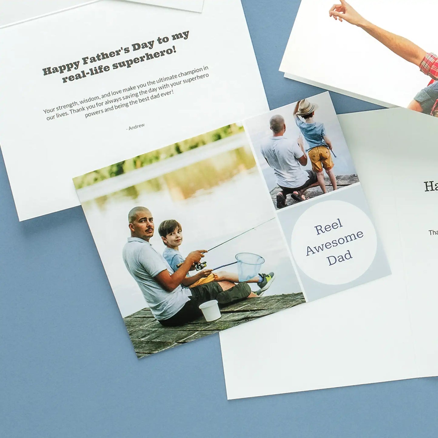 Multiple custom Father's Day cards spread across a blue surface, showing a fishing-themed 'Reel Awesome Dad' card with a photo collage of a father and son fishing on a dock, alongside other card designs featuring personalized messages
