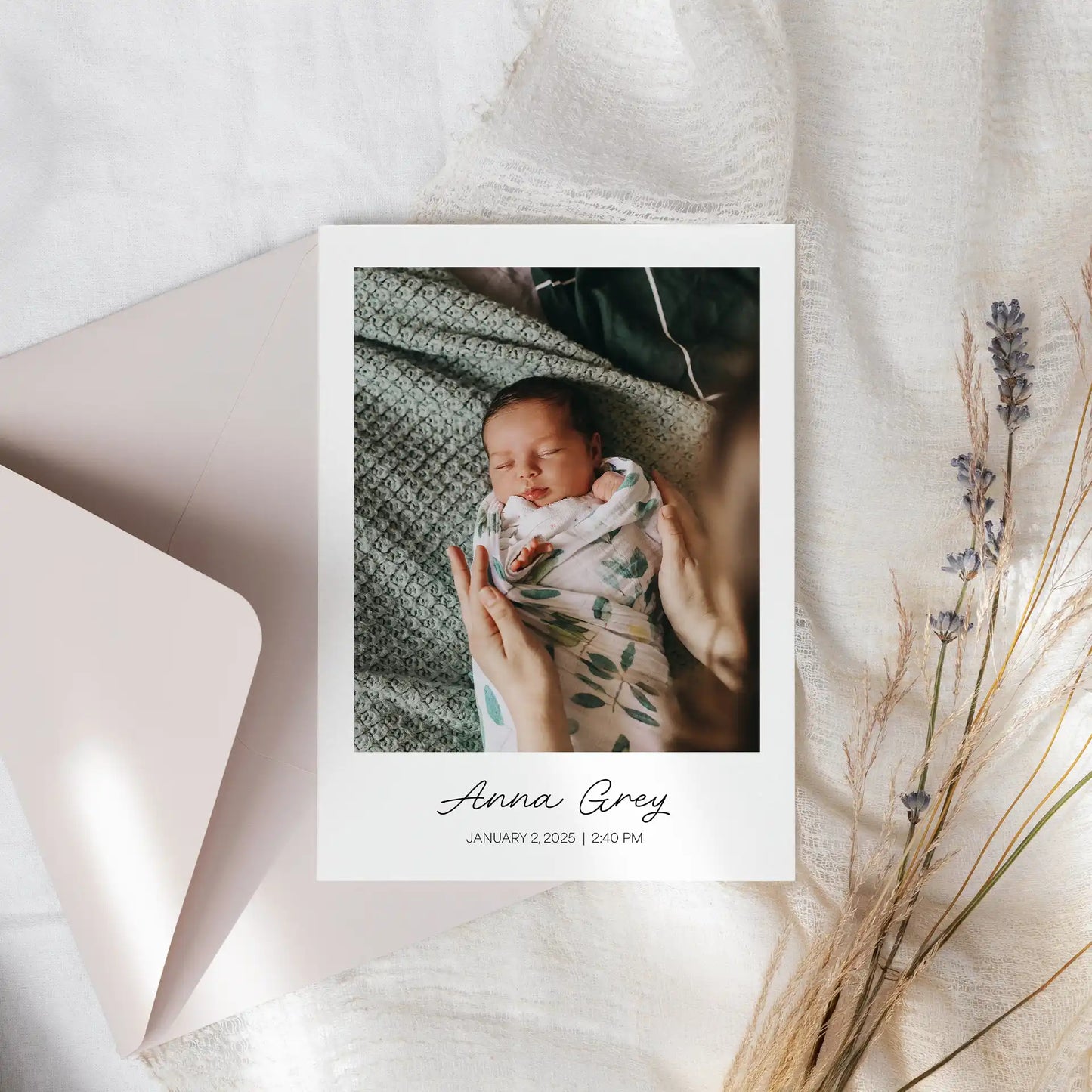 Folded birth announcement card with newborn photo, baby name and date printed below image, displayed with envelope and dried florals.