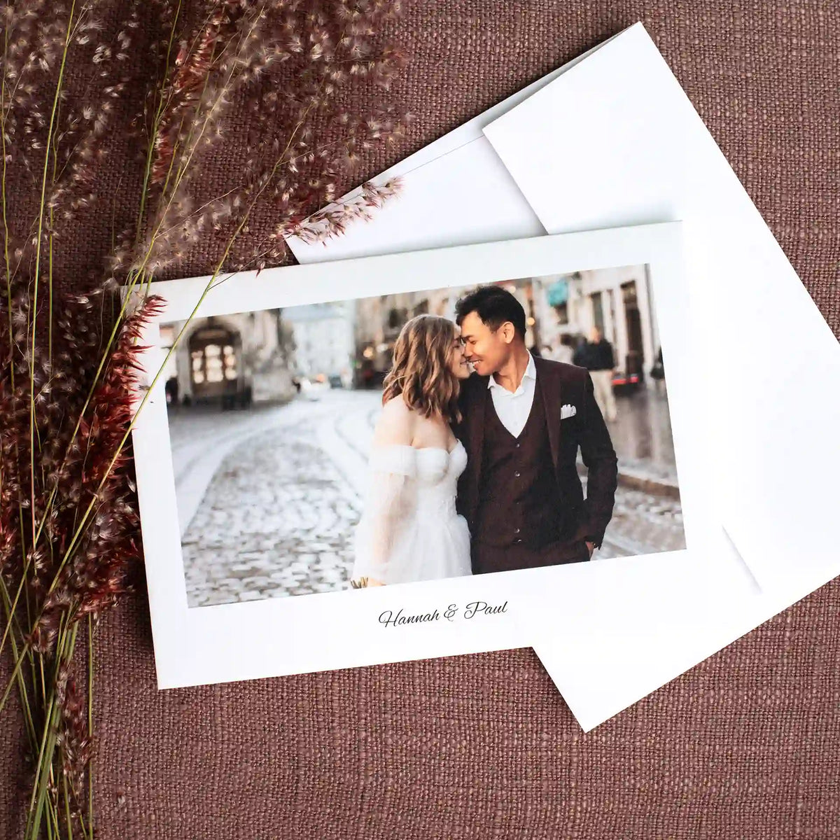 Folded thank you card featuring a bride and groom embracing on a cobblestone street, signed 'Hannah & Paul,' with matching envelope.