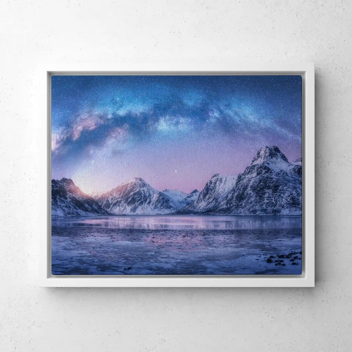 Framed canvas print with white frame showing snowy mountains and lake beneath colorful aurora sky, panoramic layout, displayed as wall art.