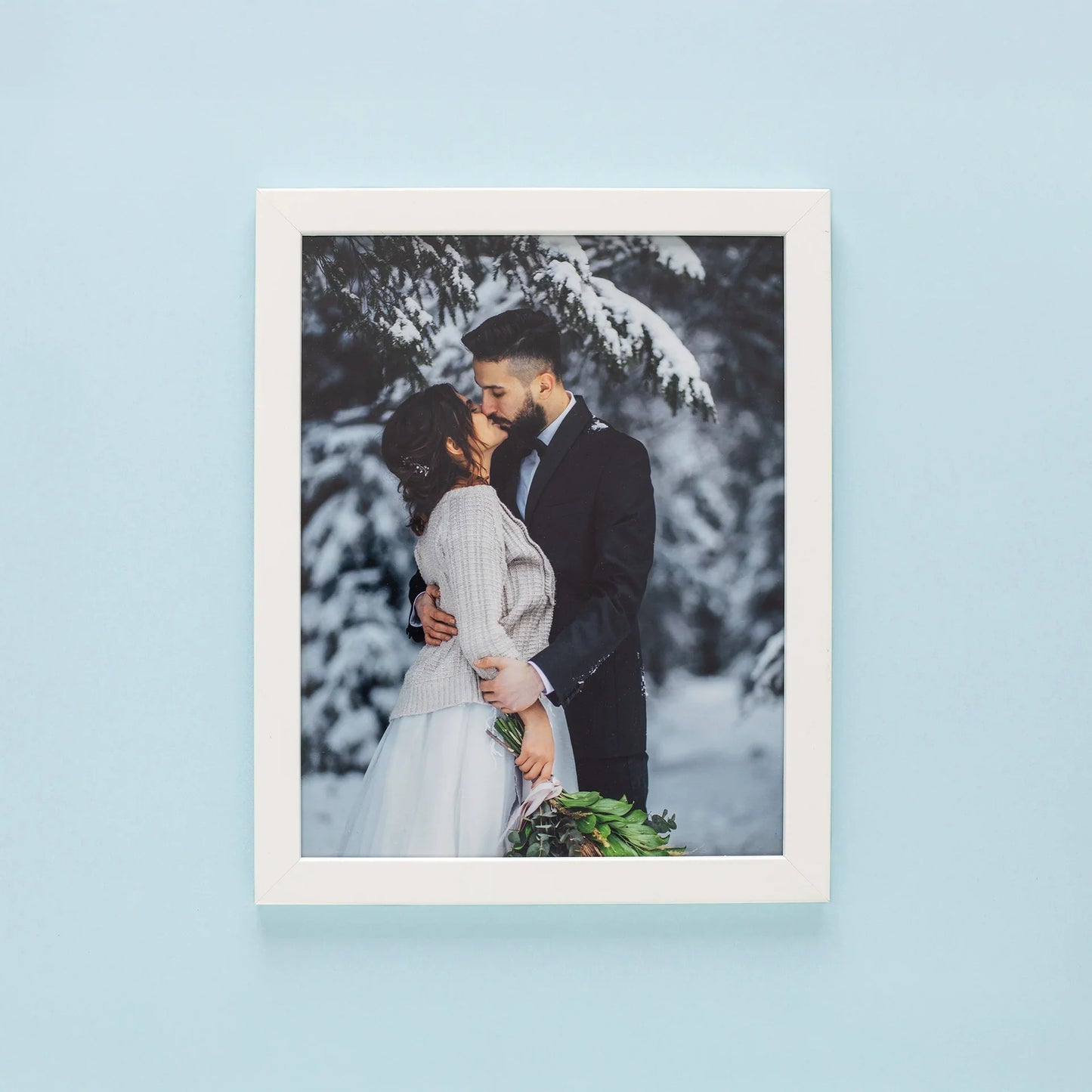 Framed print with white frame featuring couple embracing in snowy forest, vertical orientation, winter setting with trees and soft natural light.
