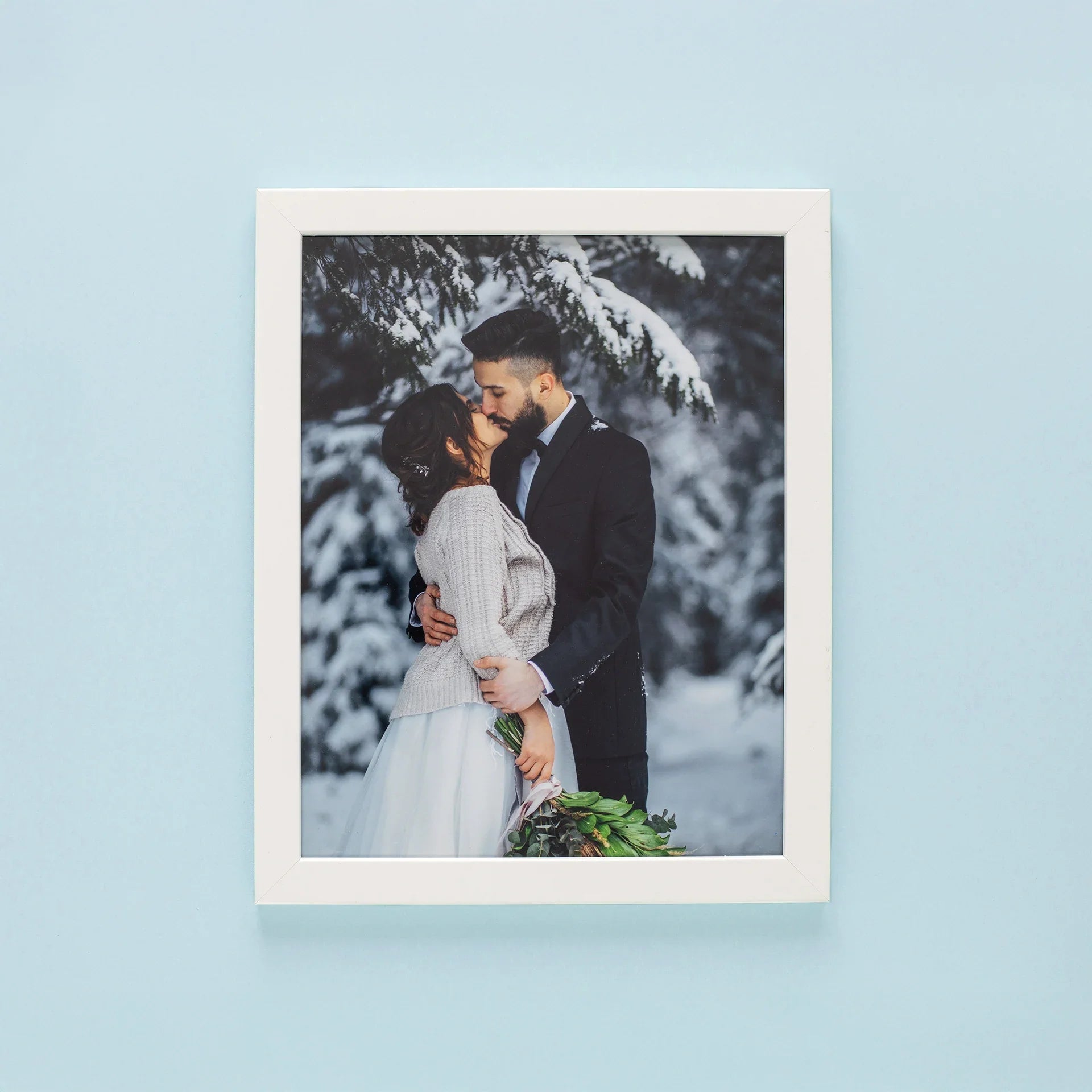Framed print with white frame featuring couple embracing in snowy forest, vertical orientation, winter setting with trees and soft natural light.