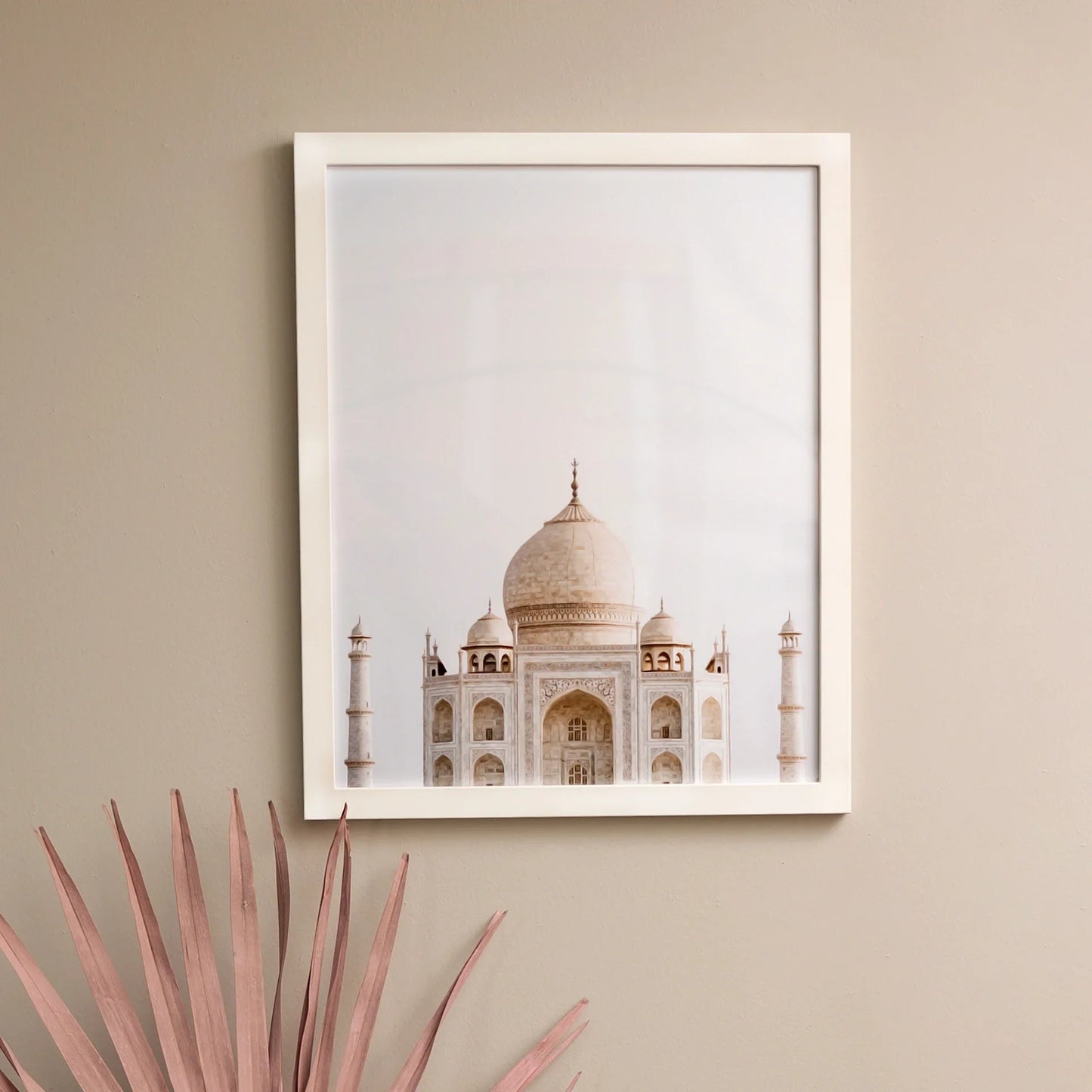 White framed square photo print of the Taj Mahal centered against a pale sky, mounted on a neutral interior wall.