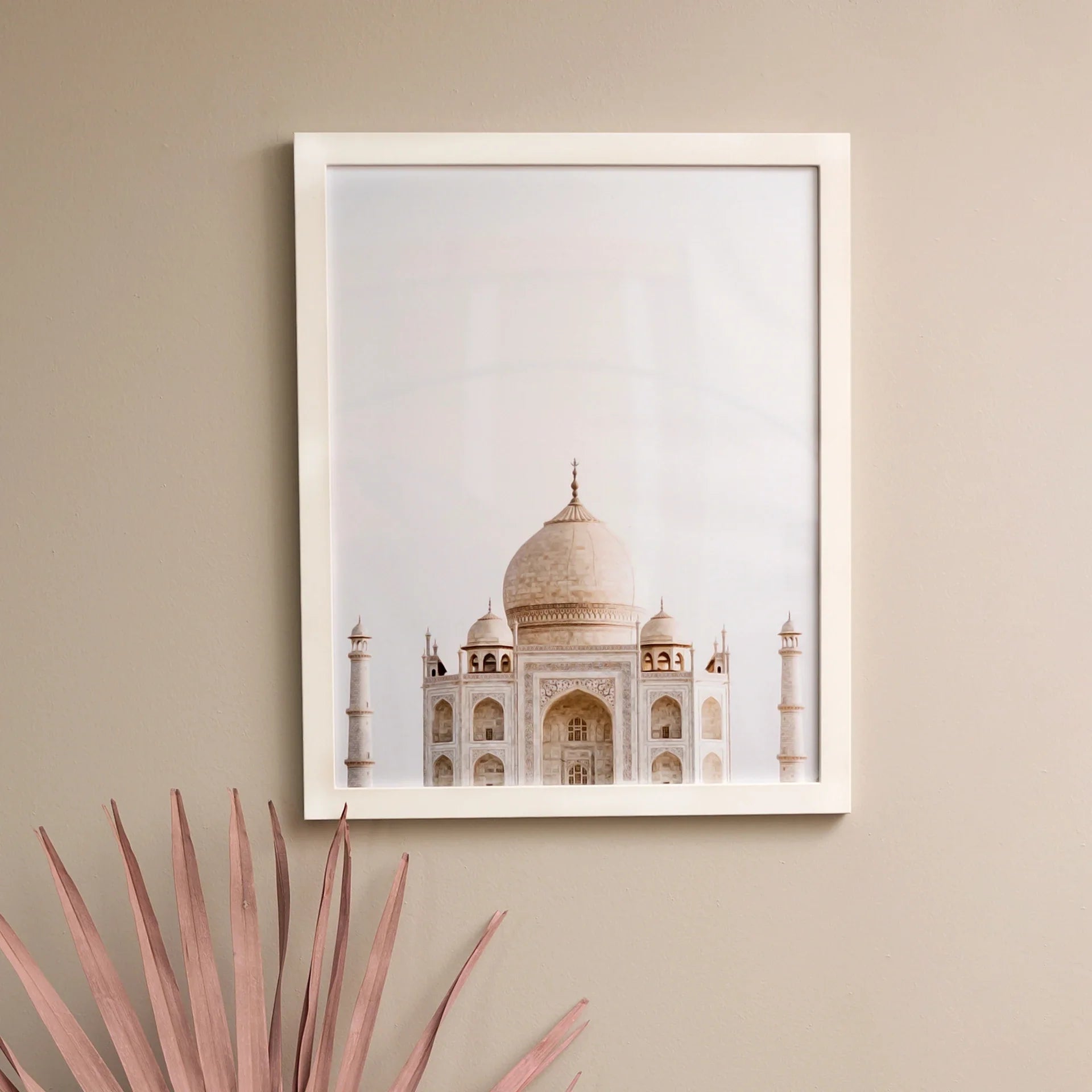 White framed square photo print of the Taj Mahal centered against a pale sky, mounted on a neutral interior wall.
