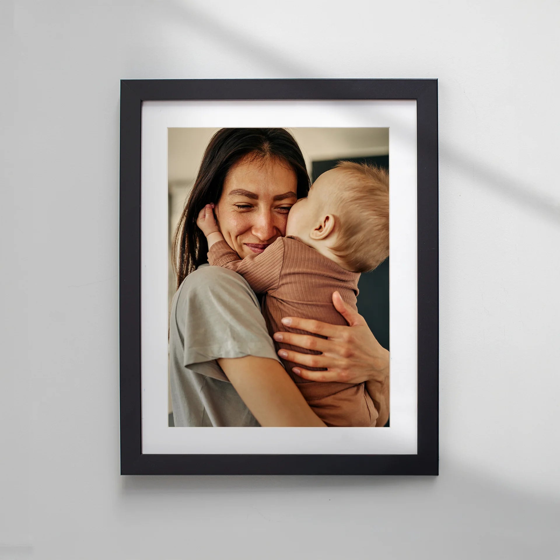 Framed photo print with a white mat, featuring a mother holding and kissing her baby.