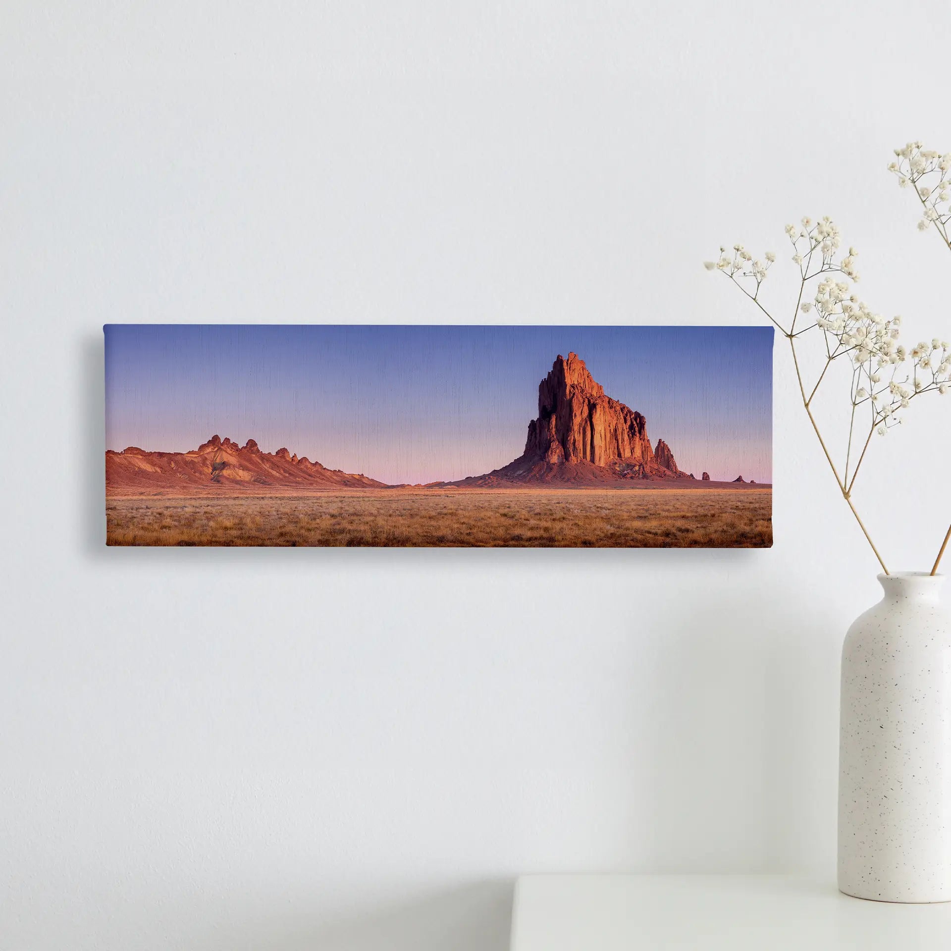 Canvas print featuring a wide desert landscape with a tall rock formation and open plains under a clear sky, displayed on a minimalist wall.