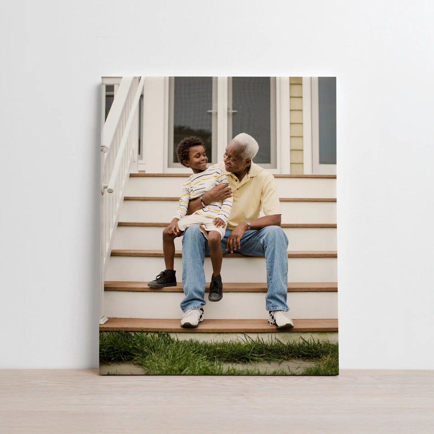 Canvas print showing an older adult and a child sitting together on outdoor steps in front of a home, smiling and interacting.