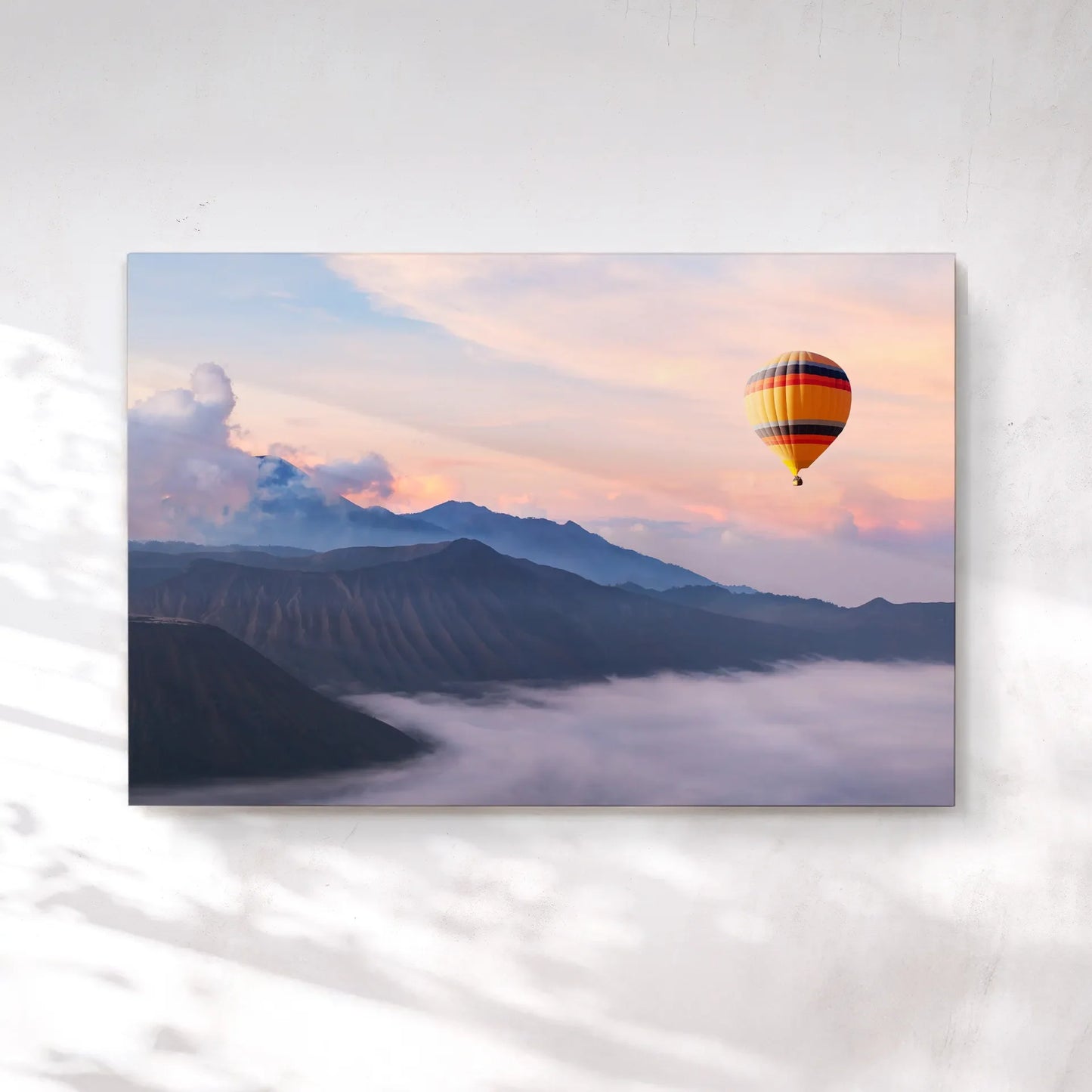 Canvas print showing a colorful hot air balloon floating above misty mountains at sunrise with soft clouds and pastel sky tones.