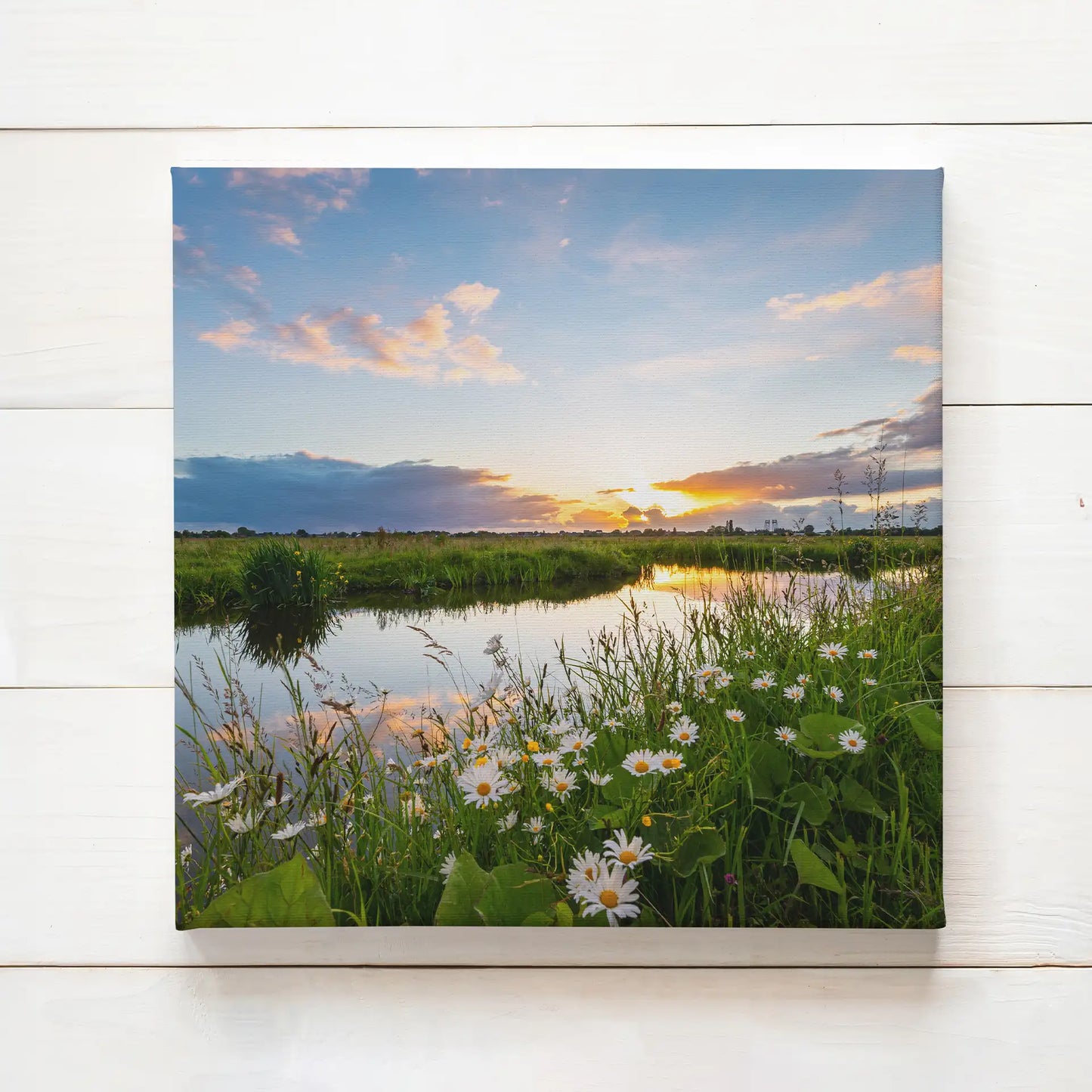 Canvas print of a peaceful riverside landscape with wildflowers, green grass, and a reflective waterway under a glowing sunset sky.