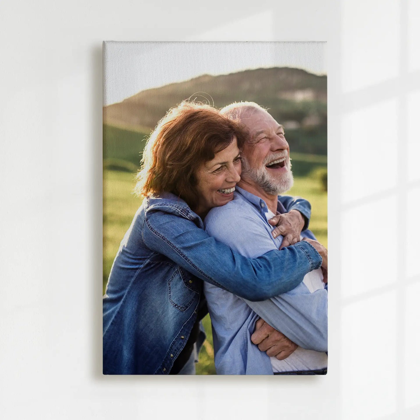 Canvas print featuring an older couple embracing and laughing outdoors, with soft sunlight and rolling hills in the background.