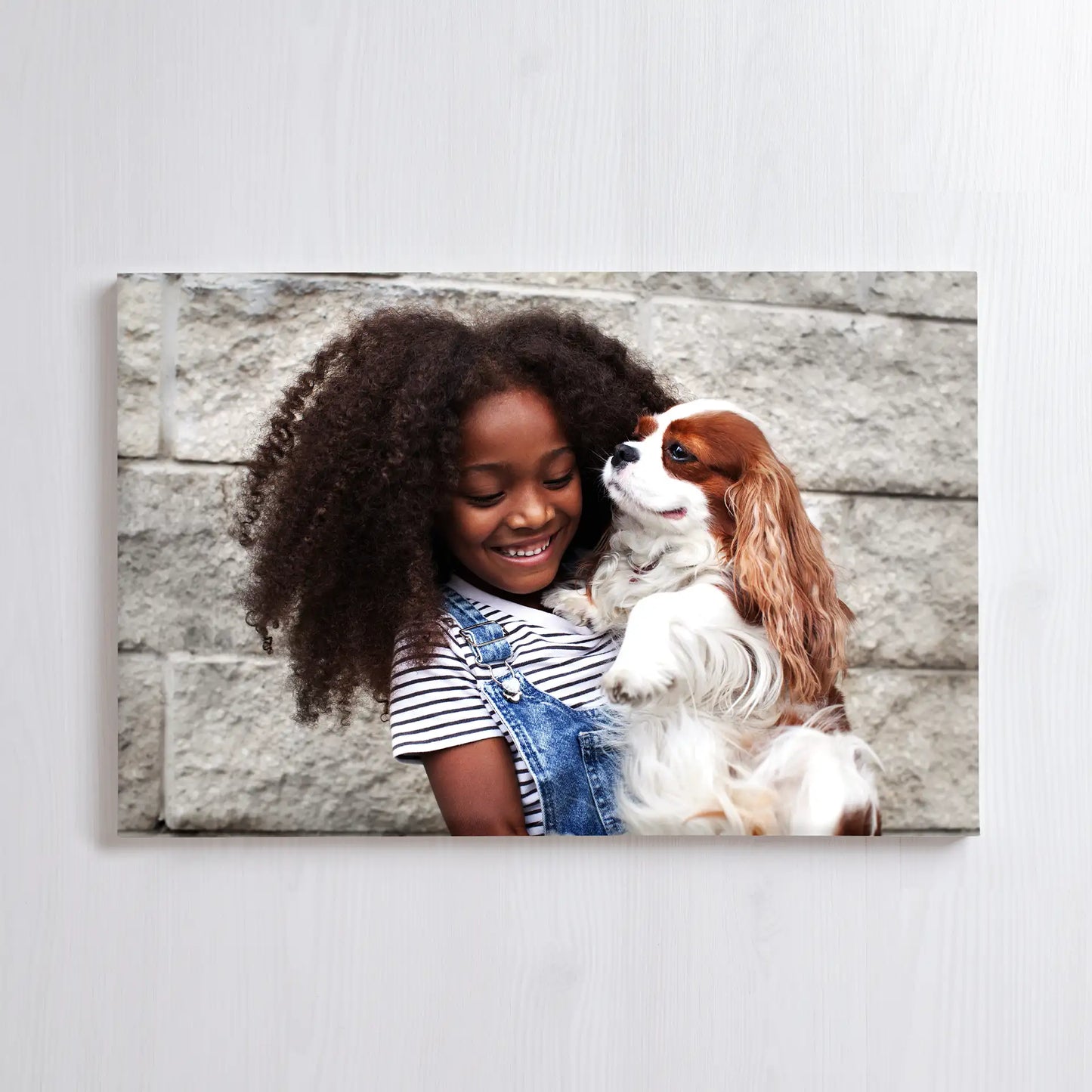 Canvas print showing a child holding a small dog, both looking at each other against a neutral stone wall background.