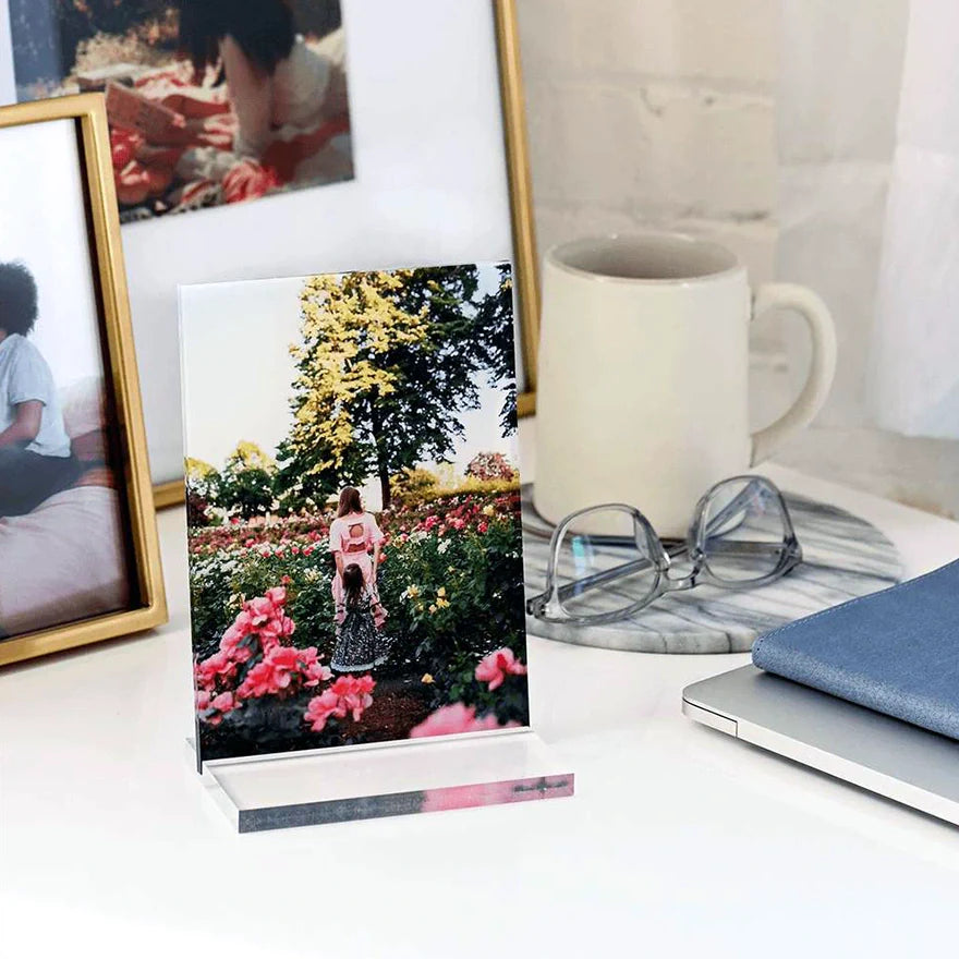 Acrylic desk print displaying a photo of a mother and child in a flower garden, set on a desk with everyday items.