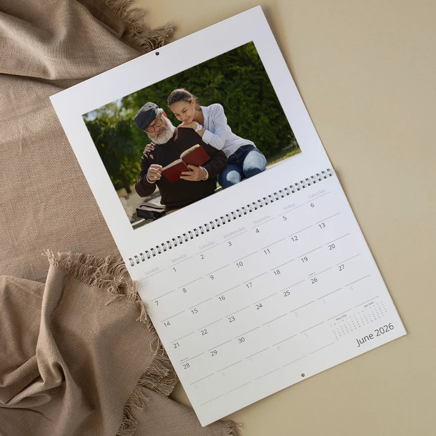 Wall calendar open to June 2026 featuring a family photo of grandfather and granddaughter reading together outdoors