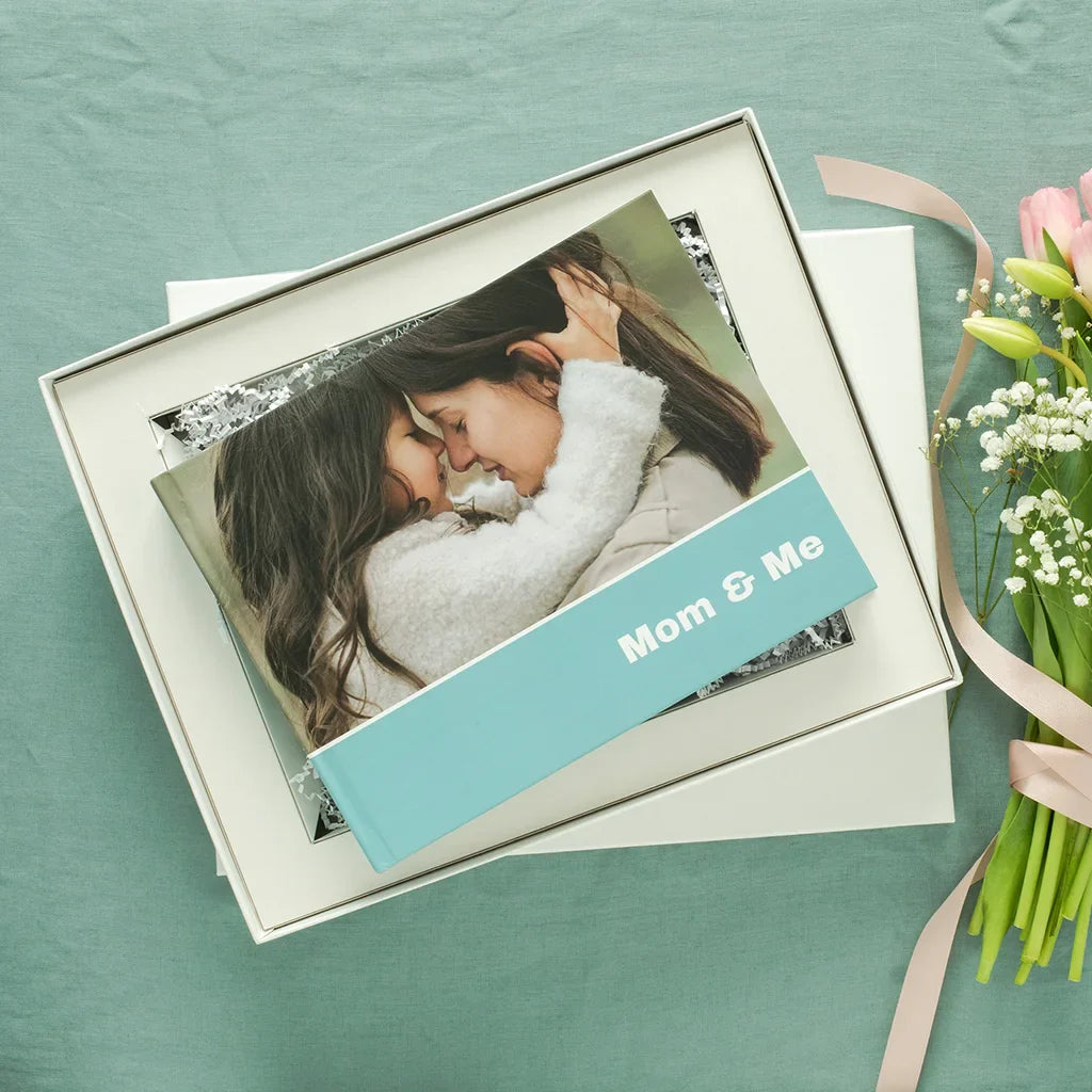 Layflat photo book presented in a gift box, featuring a mother and child on the cover with floral accents nearby.