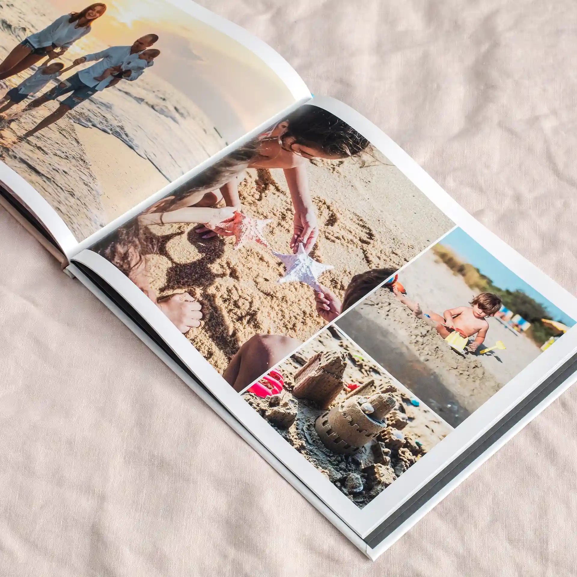 Hardcover photo book open to collage layout with multiple beach images including children playing in sand, seashells, and family moments on soft fabric surface.