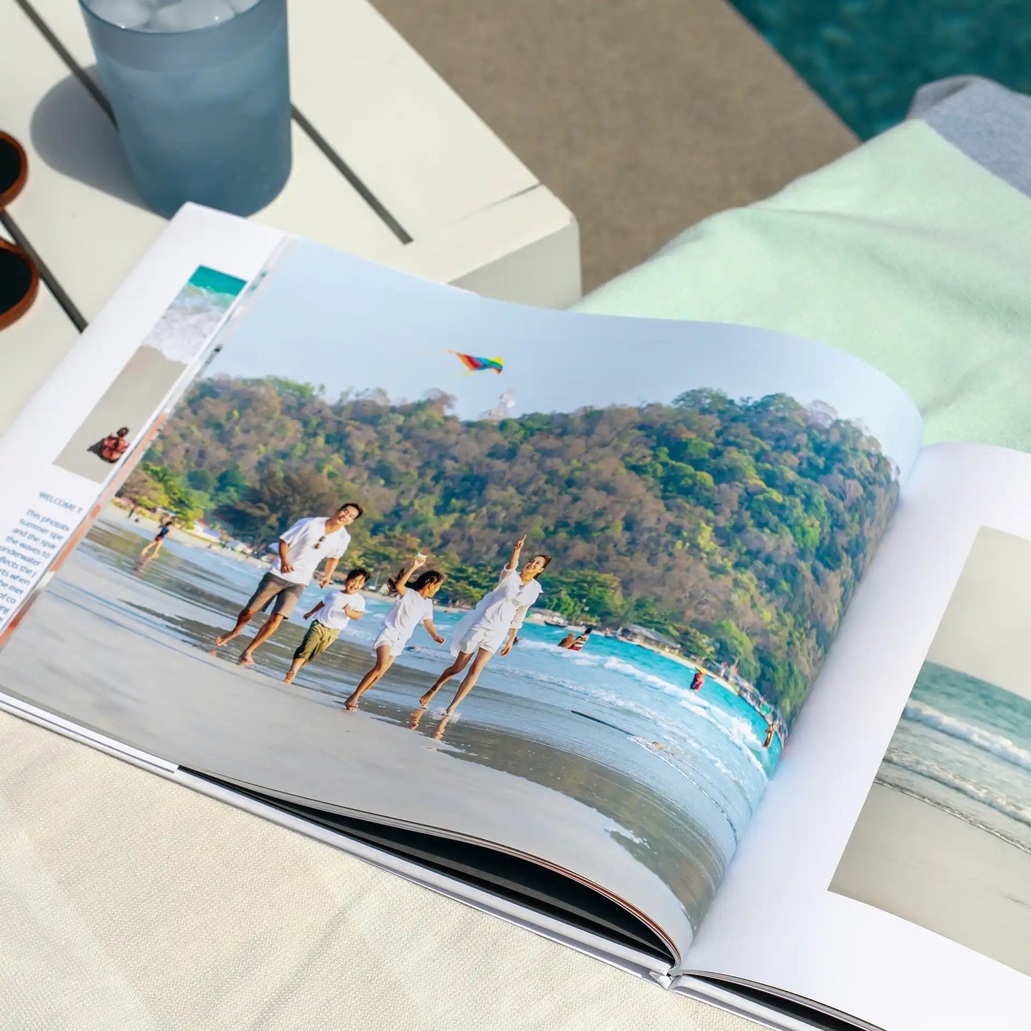 Hardcover photo book open to panoramic beach scene of family walking along shoreline, printed across seamless two-page spread on thick paper.