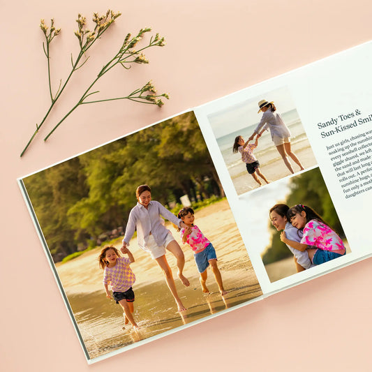 Open hardcover photo book featuring a beach-themed layout with a parent and children running along the shoreline in multiple photo frames