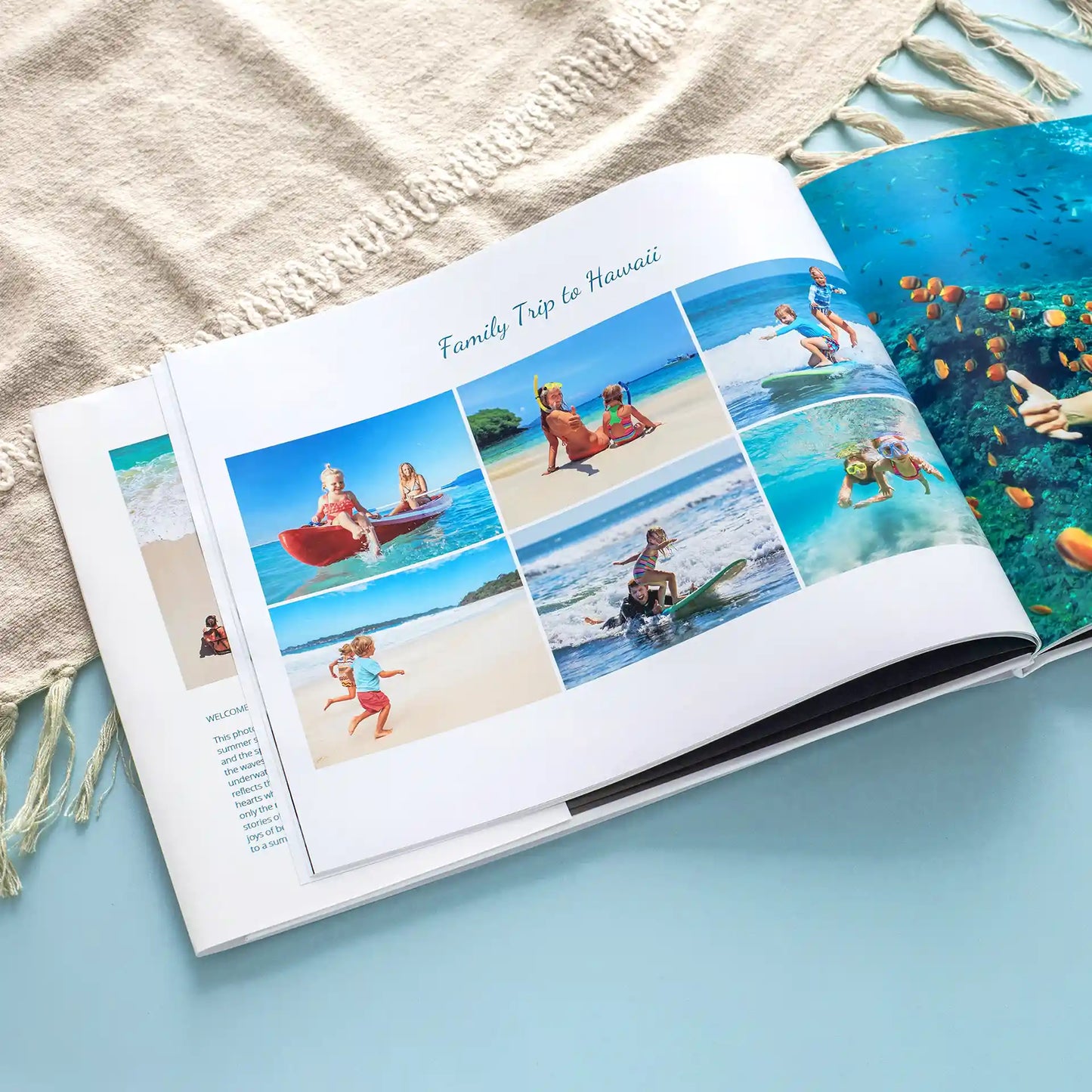 Hardcover photo book open to collage layout of beach vacation photos with multiple images arranged on white page, placed on textured towel.