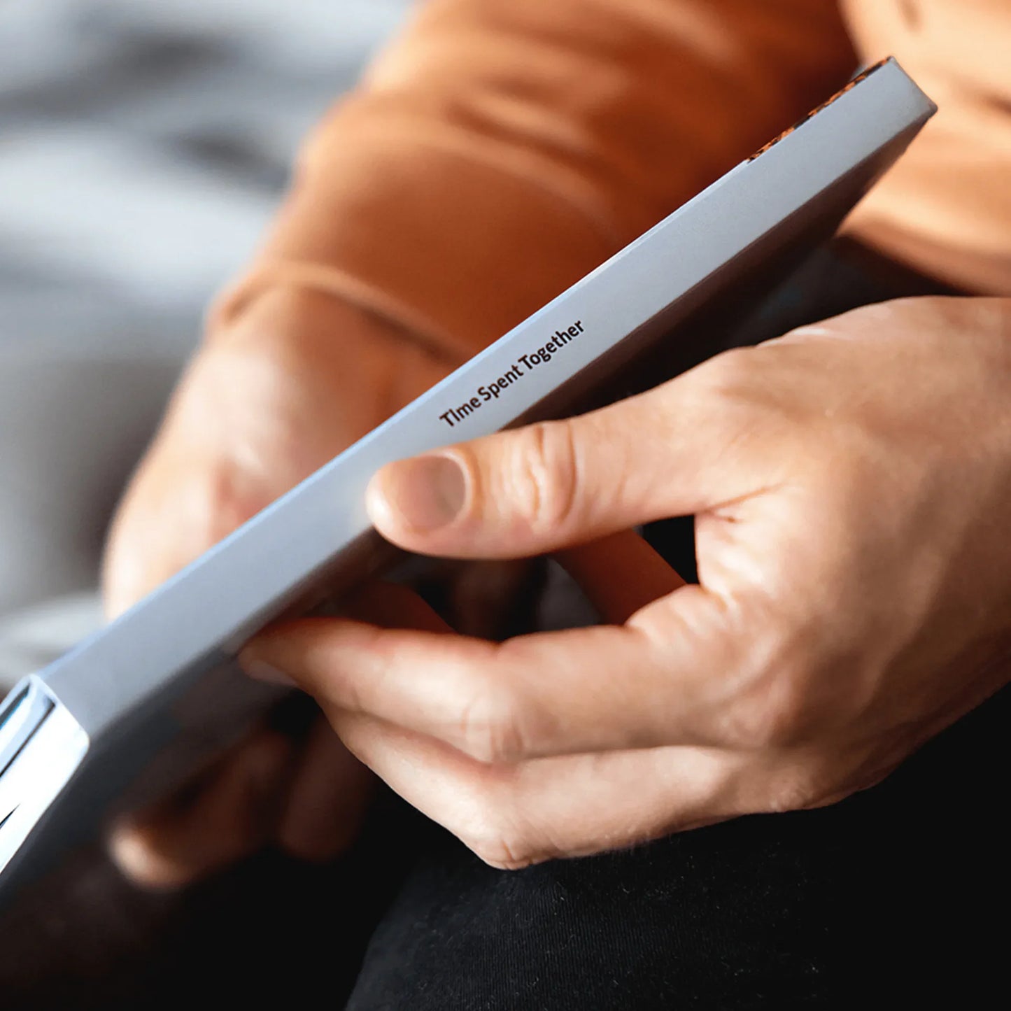 Close-up of hands holding a hardcover photo book, focusing on the spine with visible custom text printed along the edge