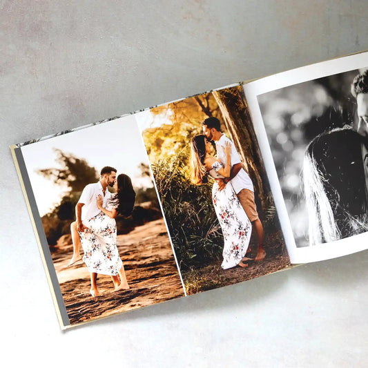 Hardcover photo book open to a three-photo spread of a couple's engagement photos in golden-hour light, including a black-and-white shot.