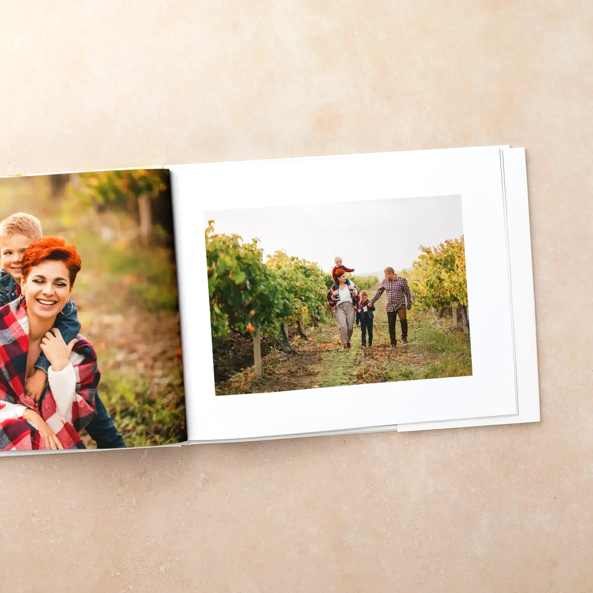 Hardcover photo book open to a white-bordered photo of a family walking through a vineyard, facing a page with a mother and son.