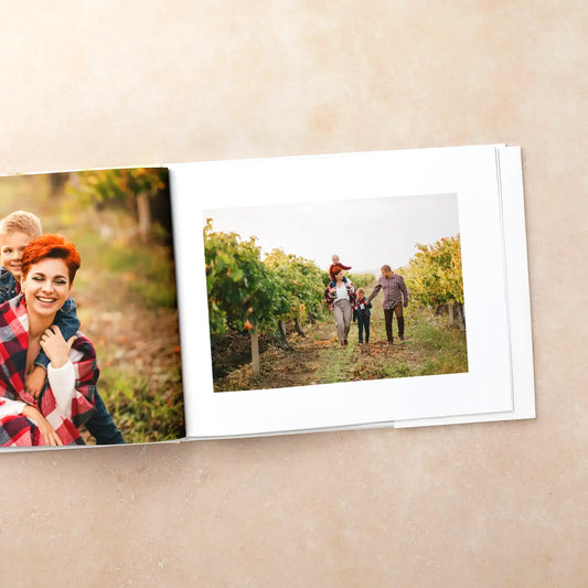 Hardcover photo book open to a white-bordered photo of a family walking through a vineyard, facing a page with a mother and son.