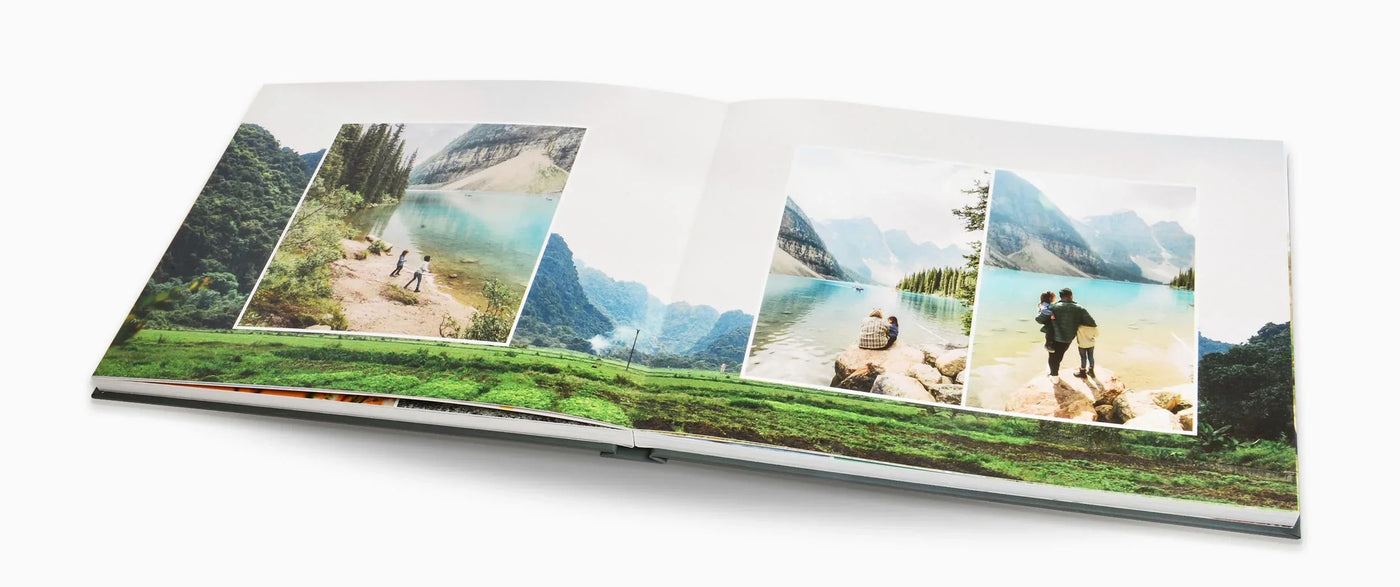 Open layflat photo book displaying travel photos of people by a turquoise mountain lake and scenic landscape spread across both pages with full-bleed background image.
