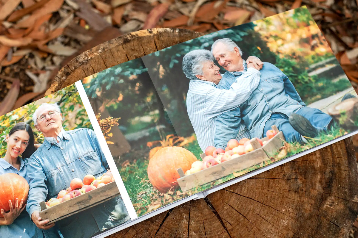 Layflat photo book resting on a tree stump, open to fall photos of grandparents embracing among pumpkins and apple crates, and a granddaughter with her grandfather holding a pumpkin.