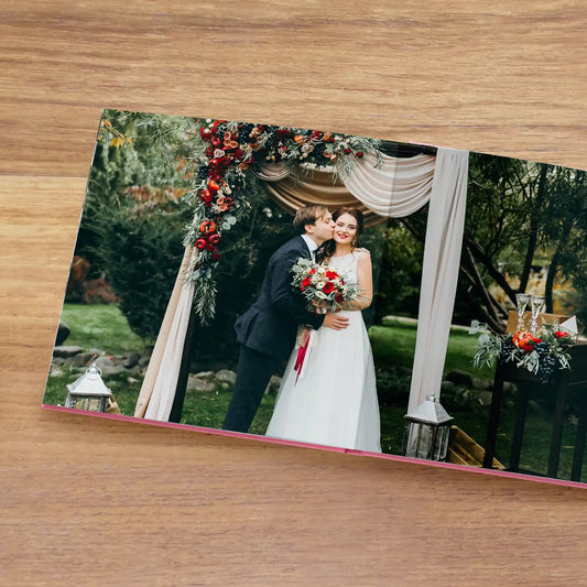Layflat photo book open to a full-spread photo of a bride and groom kissing under a floral wedding arch.