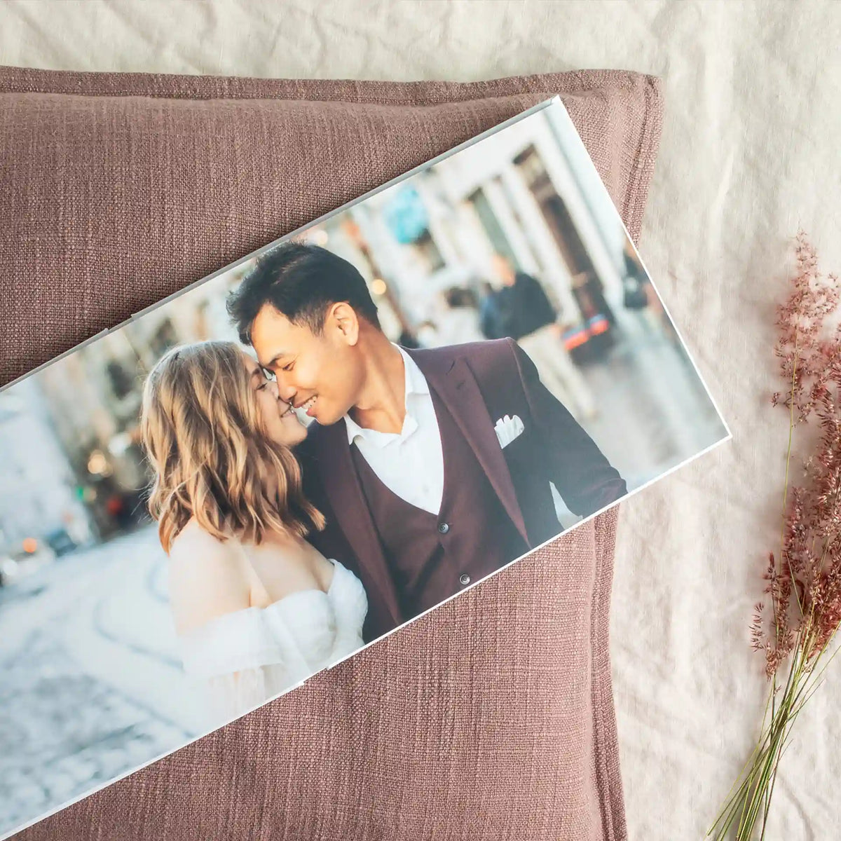 Layflat photo book open to a panoramic engagement photo of a wedding couple kissing on a city street, resting on a linen-covered cushion.