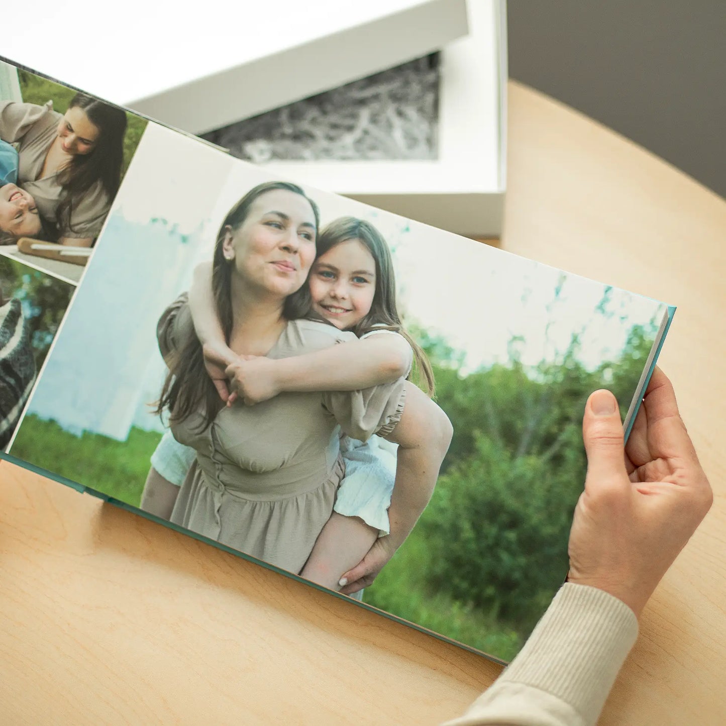 Layflat photo book held open to full-bleed family photos, showing a person and child embracing outdoors, highlighting crease-free panoramic pages.