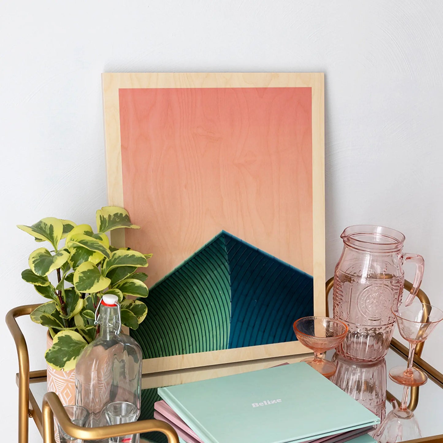 Maple wood print featuring coral and teal abstract design with visible wood grain border, displayed on a bar cart with glassware and houseplants.