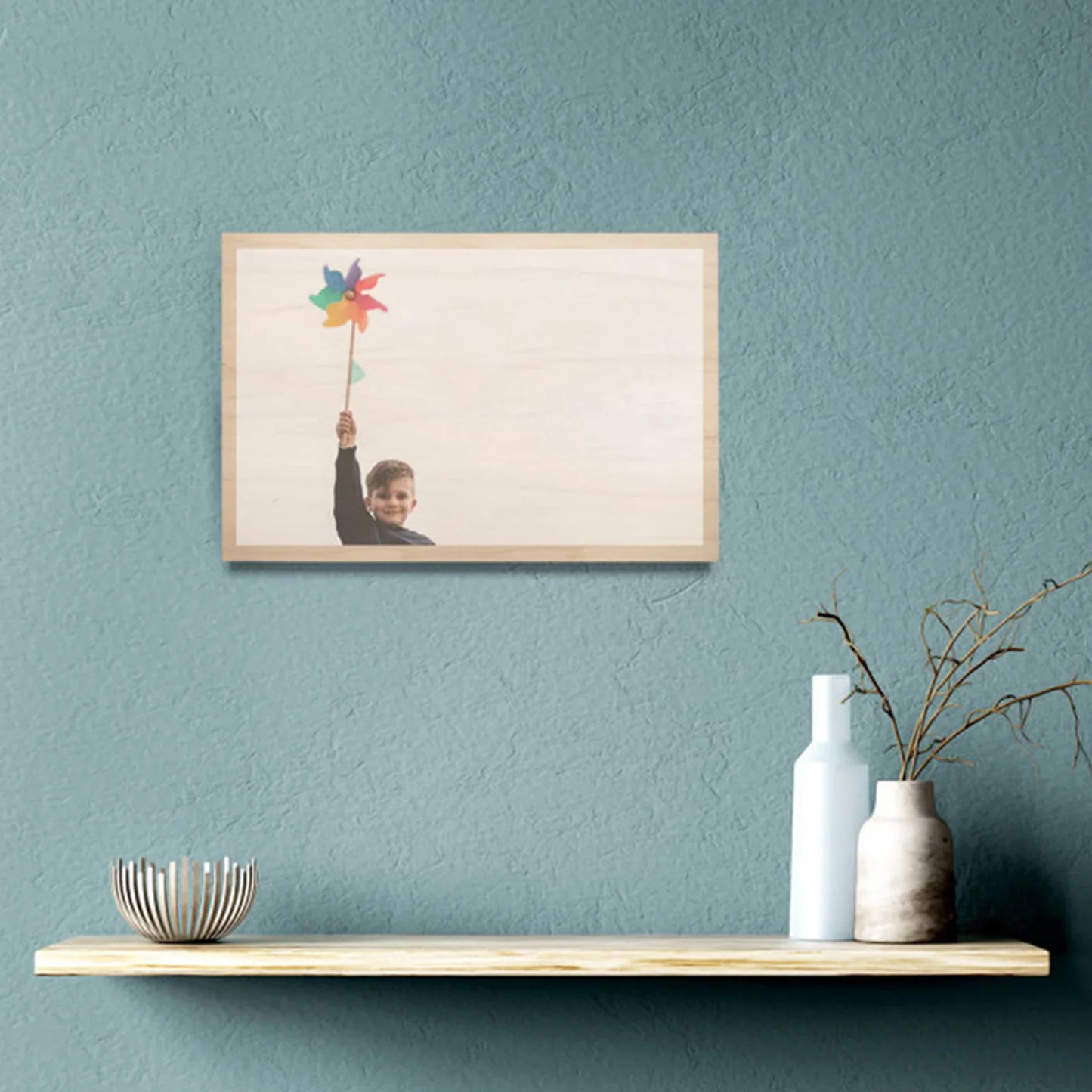 Maple wood print with light wood finish featuring child holding colorful pinwheel against sky, horizontal orientation, displayed on wall above floating shelf.